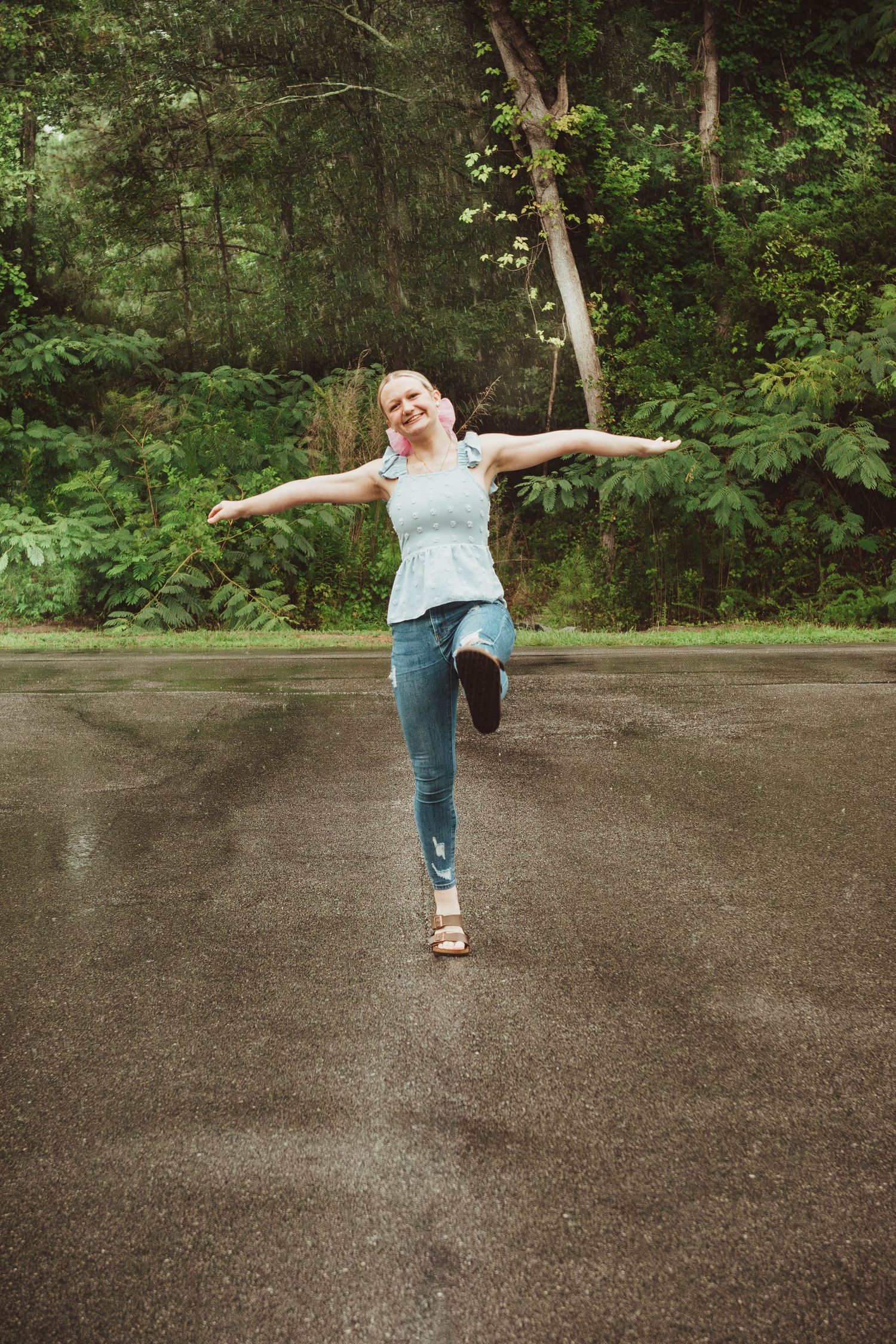 A joyful figure dances on a wet pavement path surrounded by lush green forest scenery.