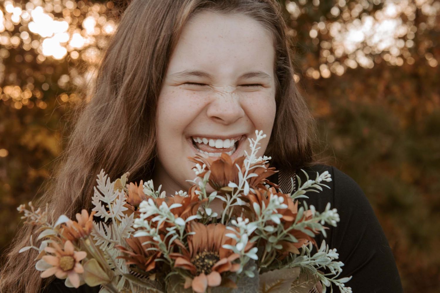 A joyful expression shown through genuine laughter while holding a natural bouquet of muted floral blooms at sunset.