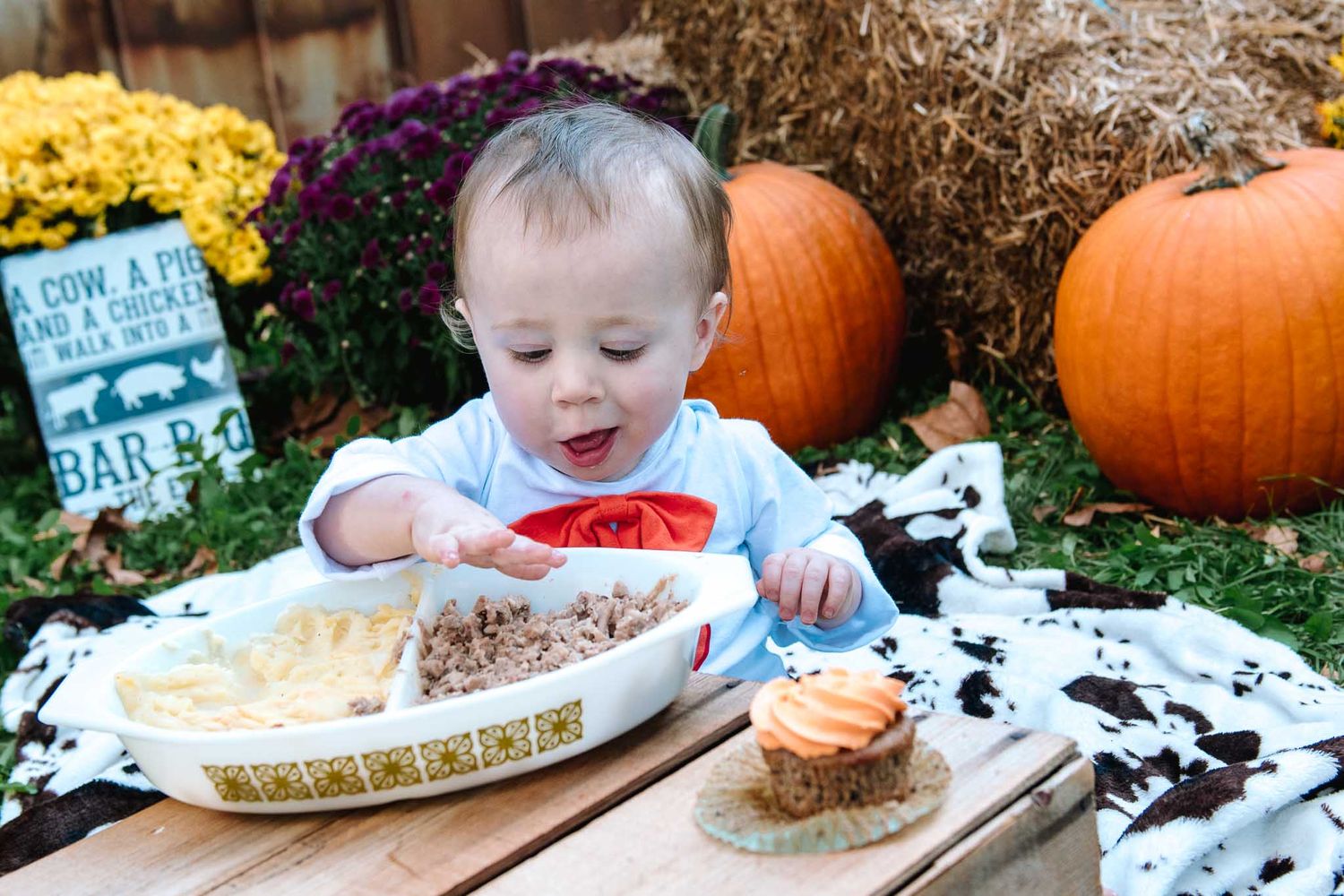 Fall harvest scene with someone trying pie at a rustic outdoor table surrounded by pumpkins and mums.