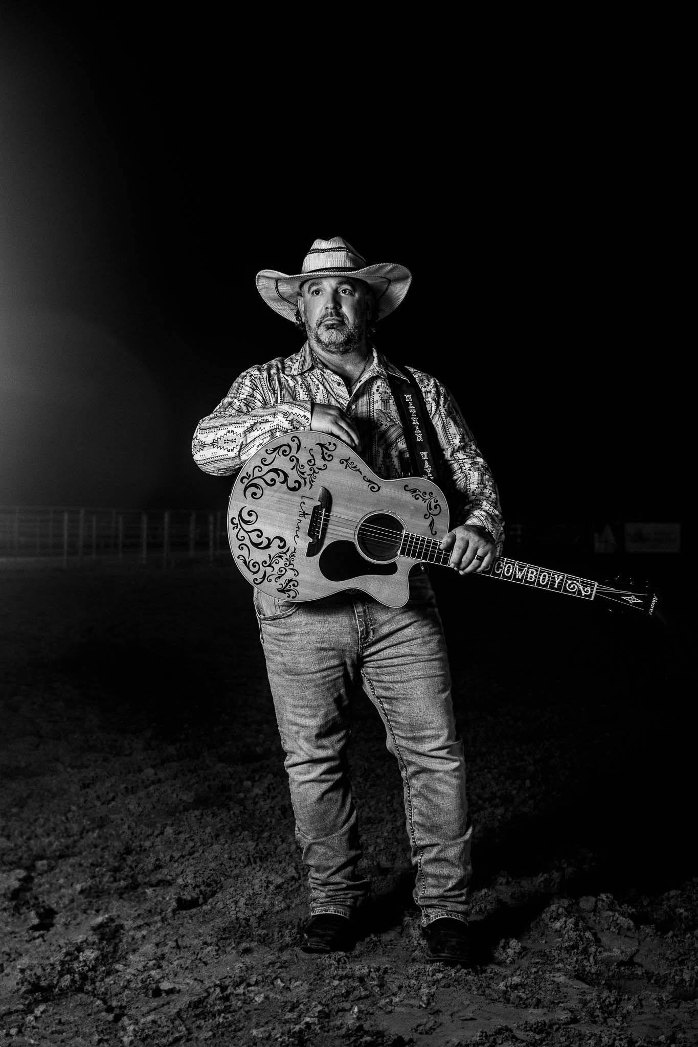 A black and white photo of a country musician wearing an embroidered shirt and cowboy hat while holding an acoustic guitar.
