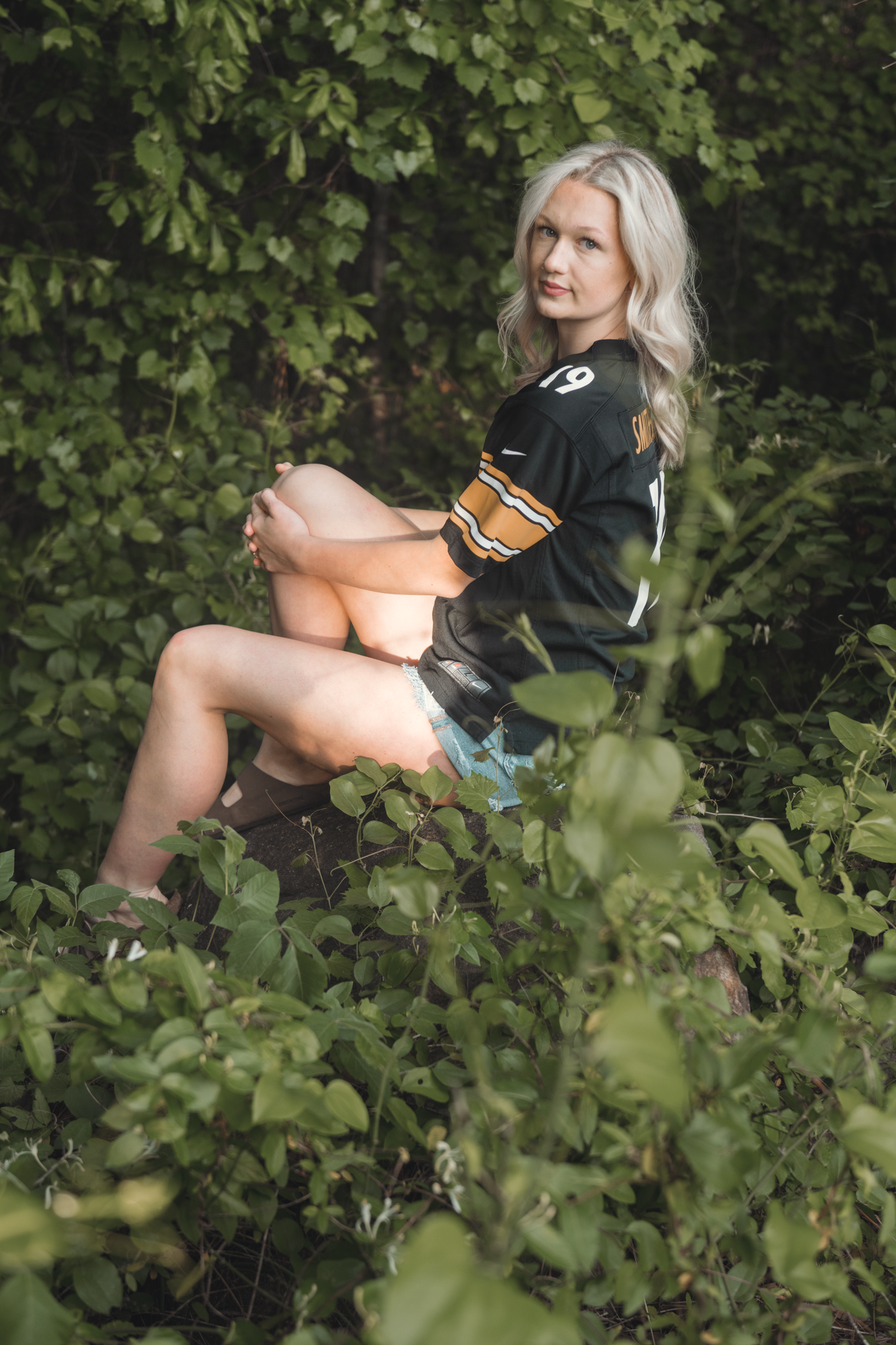 Person in black Anaheim Ducks hockey jersey sitting on tree branch surrounded by green foliage in outdoor setting.