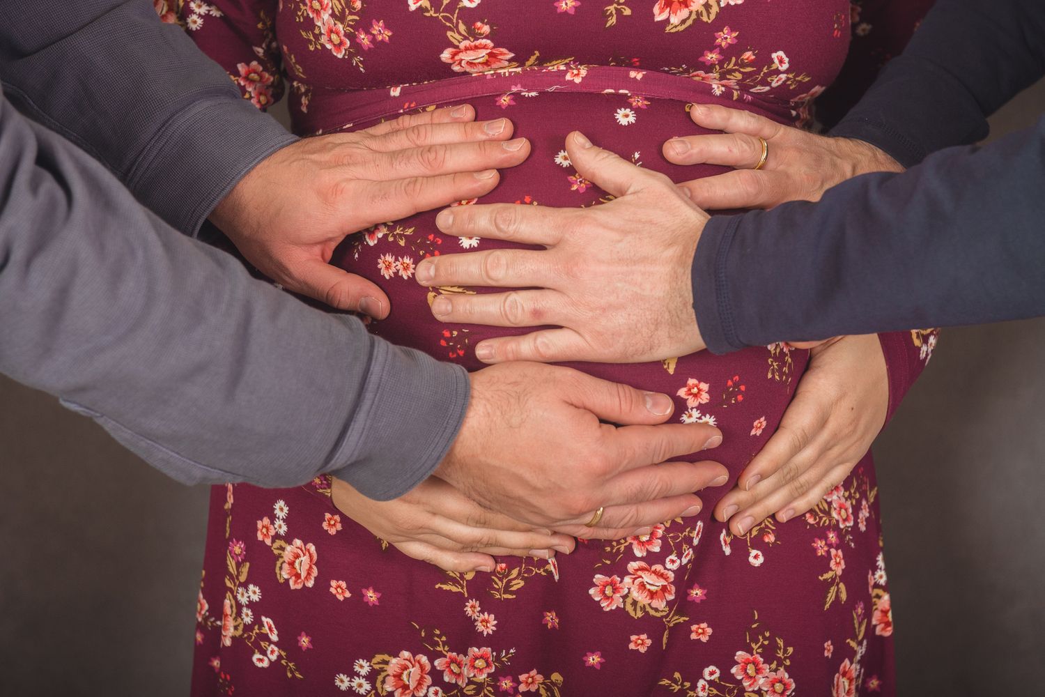 Close-up view of hands wearing engagement rings on a burgundy floral dress showing different angles and details.