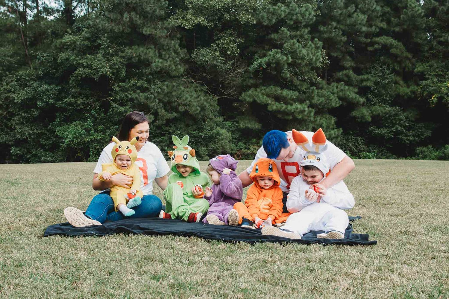 A group wearing colorful Care Bears costumes posing together on a blanket in a grassy field.