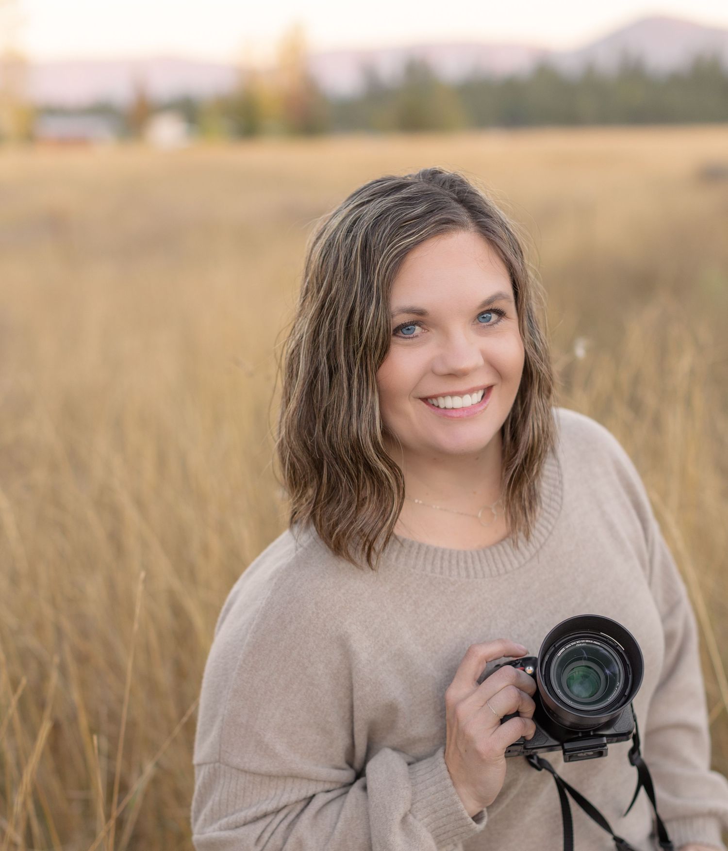Photographer with a professional camera smiling in a golden wheat field at sunset.