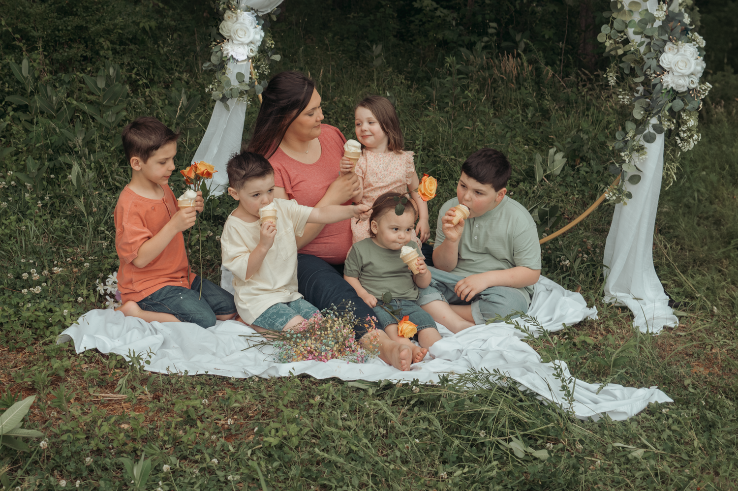 Family enjoying an outdoor picnic together on a white blanket with decorative arches in a garden setting.