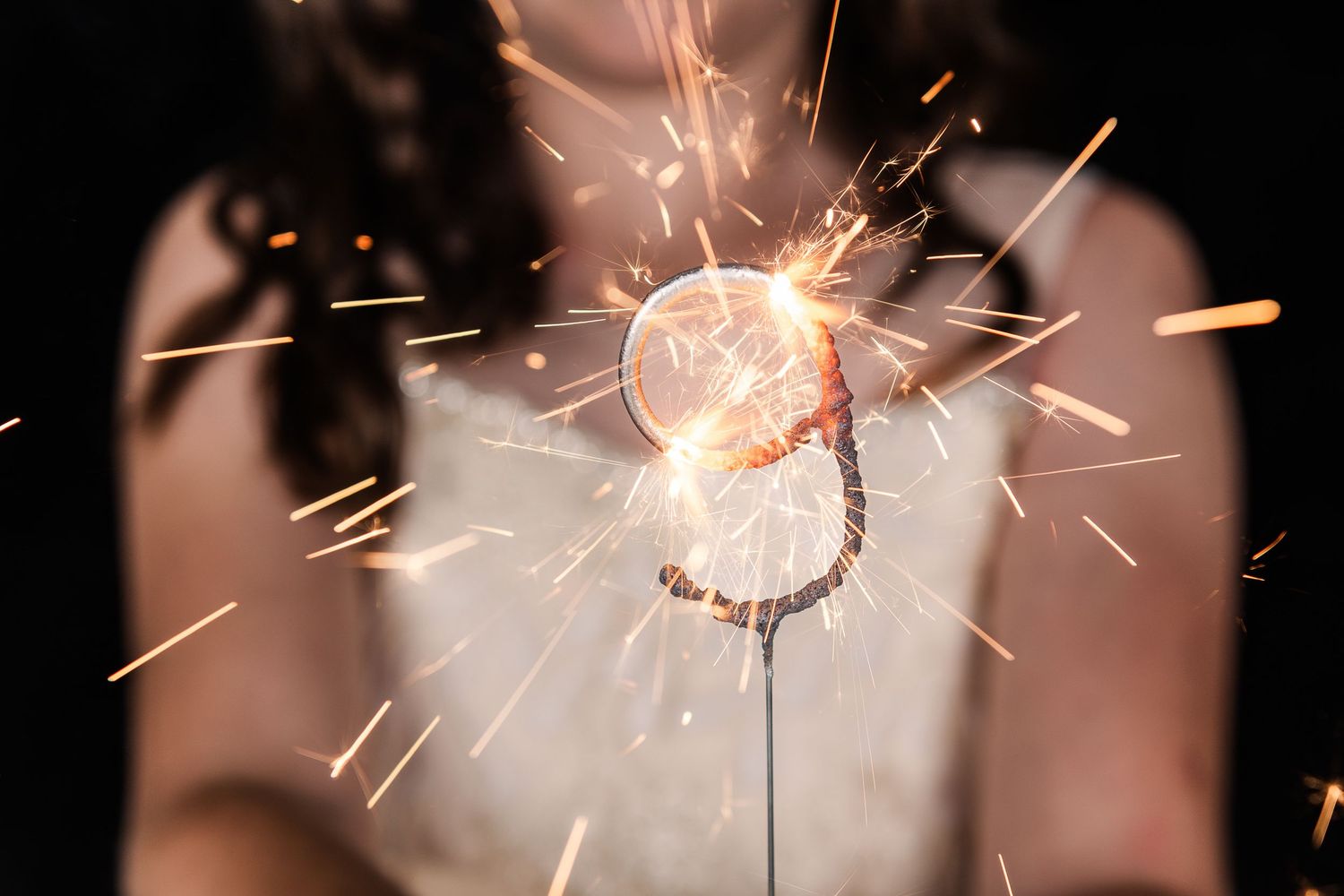 A heart-shaped sparkler creates a glowing display of sparks against a dark background in soft focus.