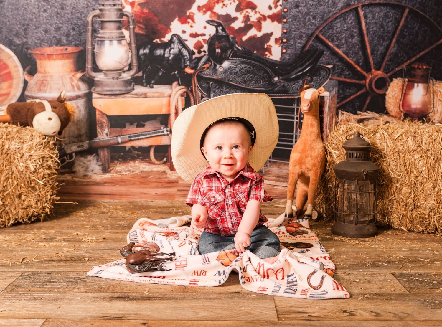 A rustic western themed photoshoot setup with hay bales, lantern, and cowboy decor against a wooden backdrop.