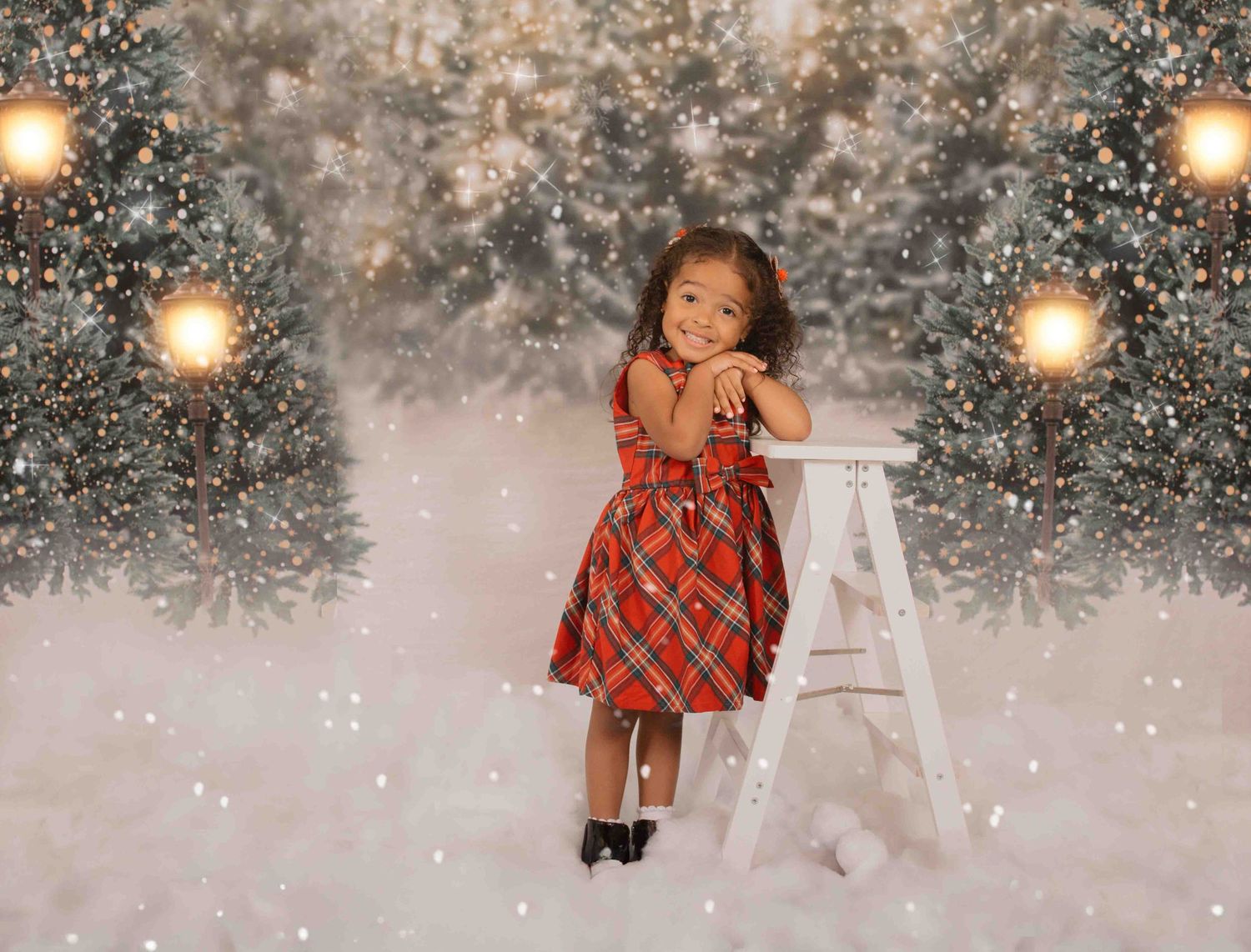 Child in red plaid holiday dress poses among snowy winter scene with glowing lights and Christmas trees.