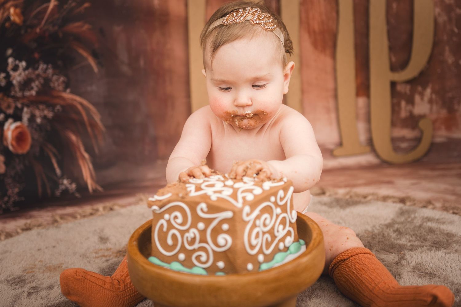 A joyful smash cake photo session featuring an ornately decorated brown and turquoise cake with white frosting details.