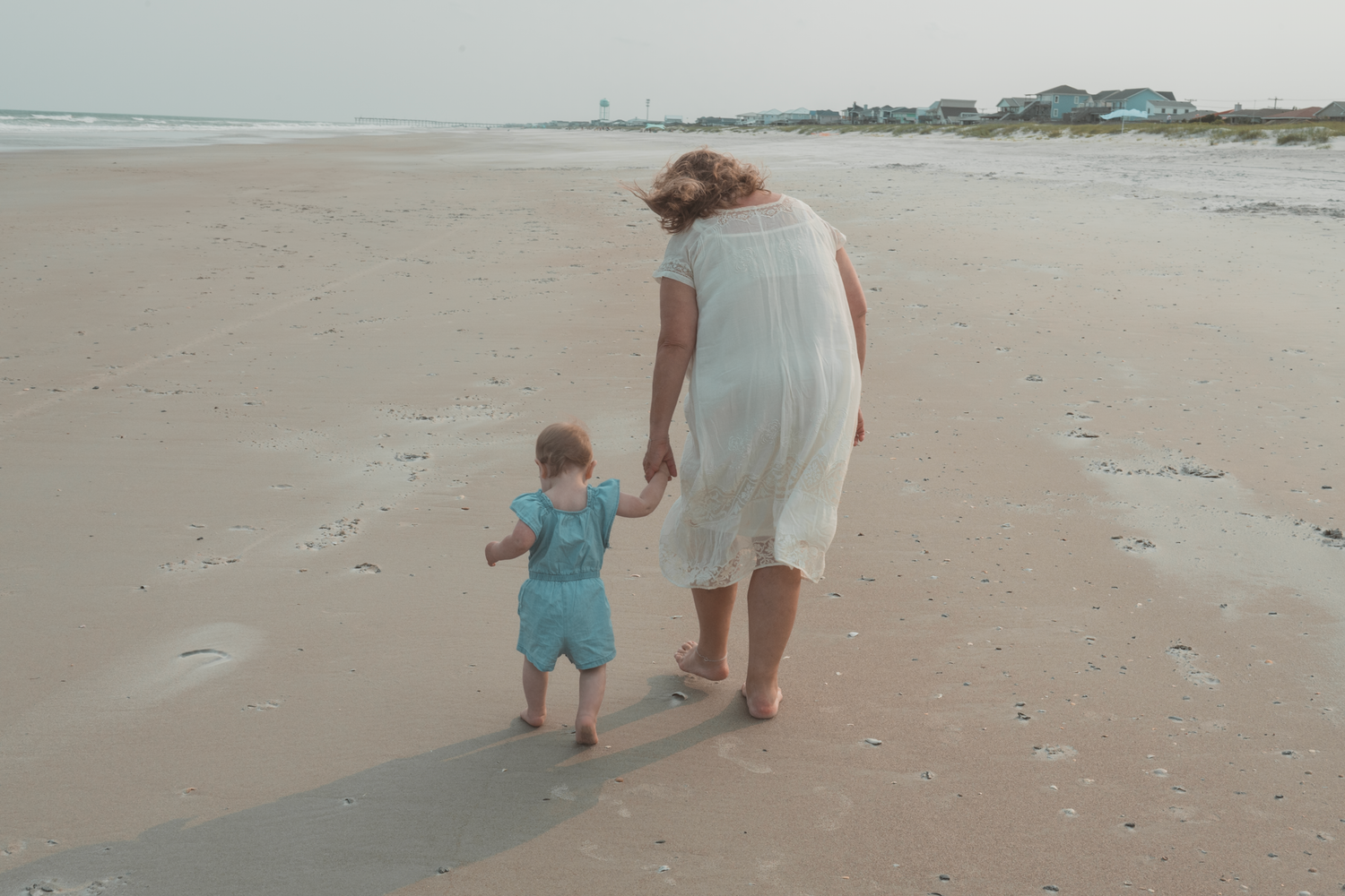 A tender moment shared between parent and child holding hands while walking along a misty beach shore.