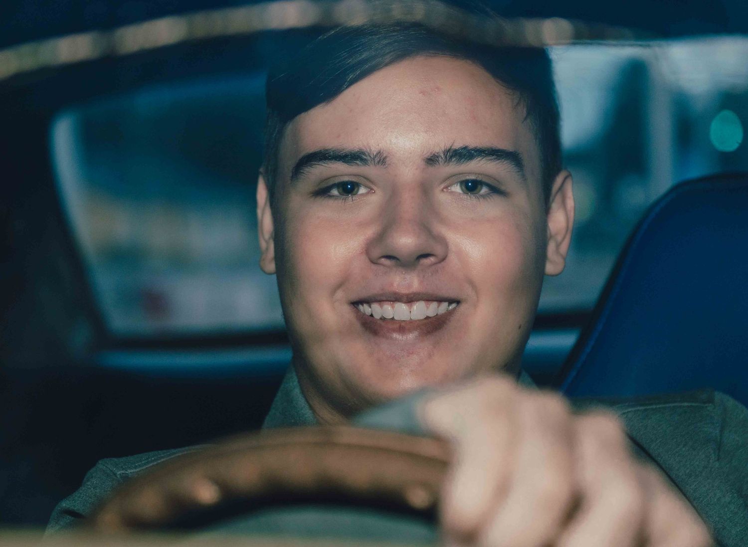 Young person smiling while sitting in driver's seat of car interior with natural lighting.