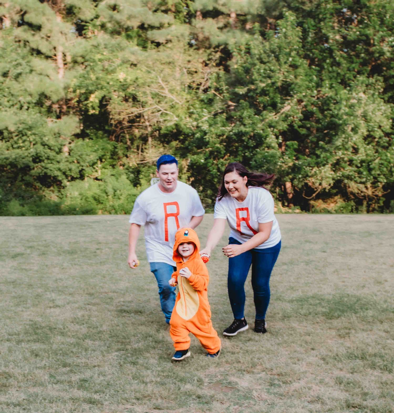 A family group wearing matching grey shirts and an orange outfit plays together in a grassy field on a sunny day.