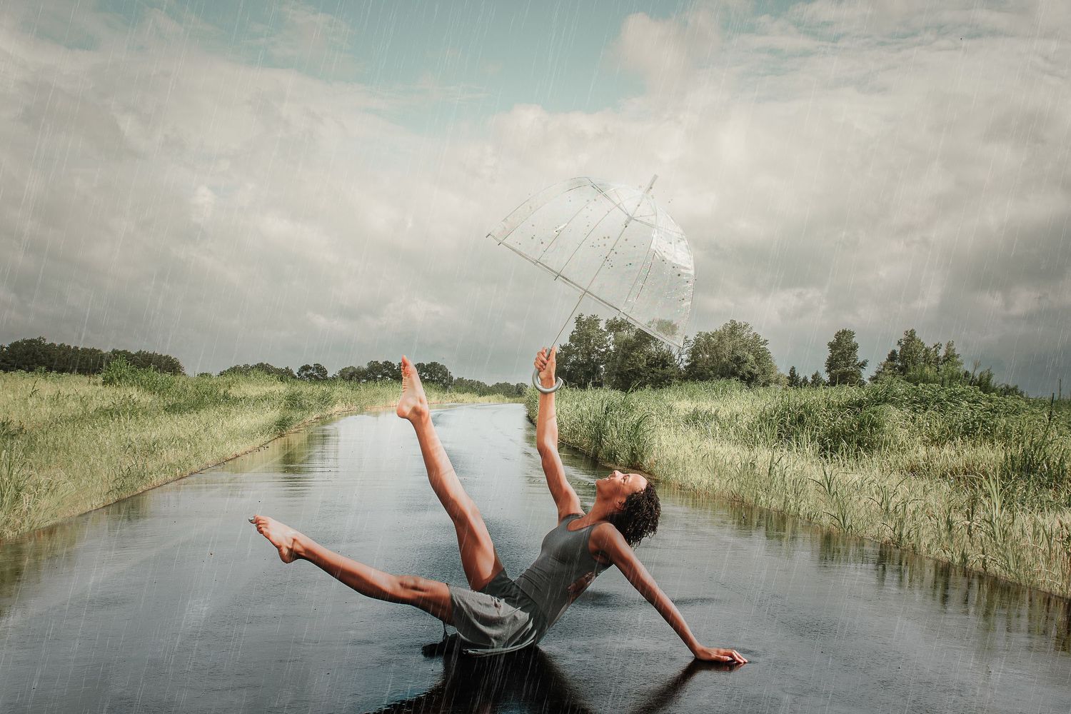 A person performs a dramatic backflip over a scenic waterway surrounded by lush green marshland and cloudy skies.