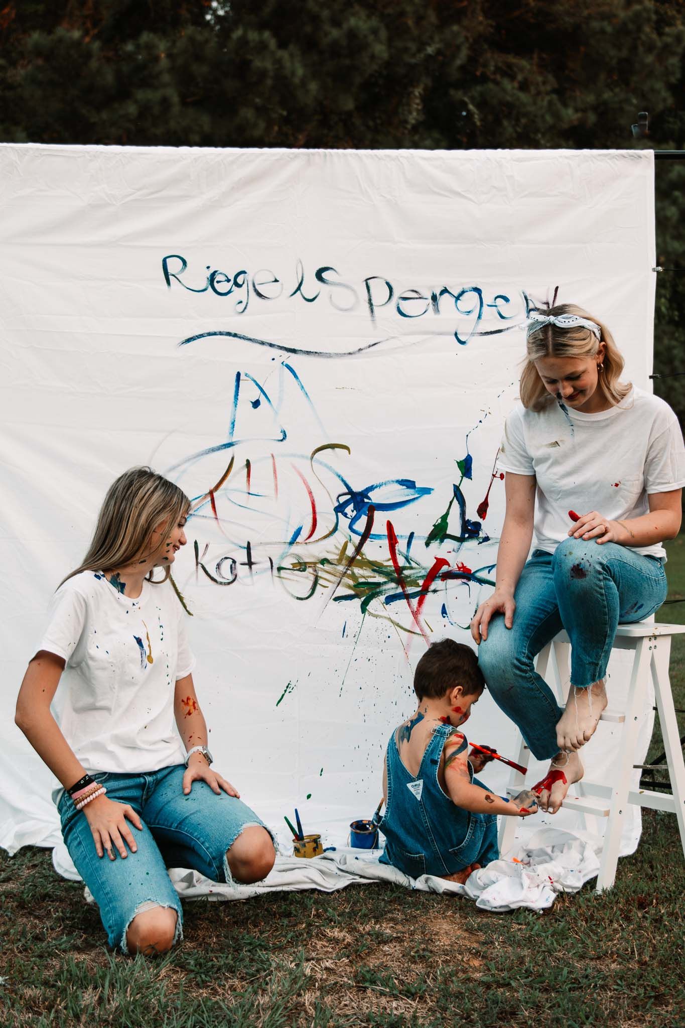 Group paints together on white backdrop with fun splashes of color outdoors on grass.