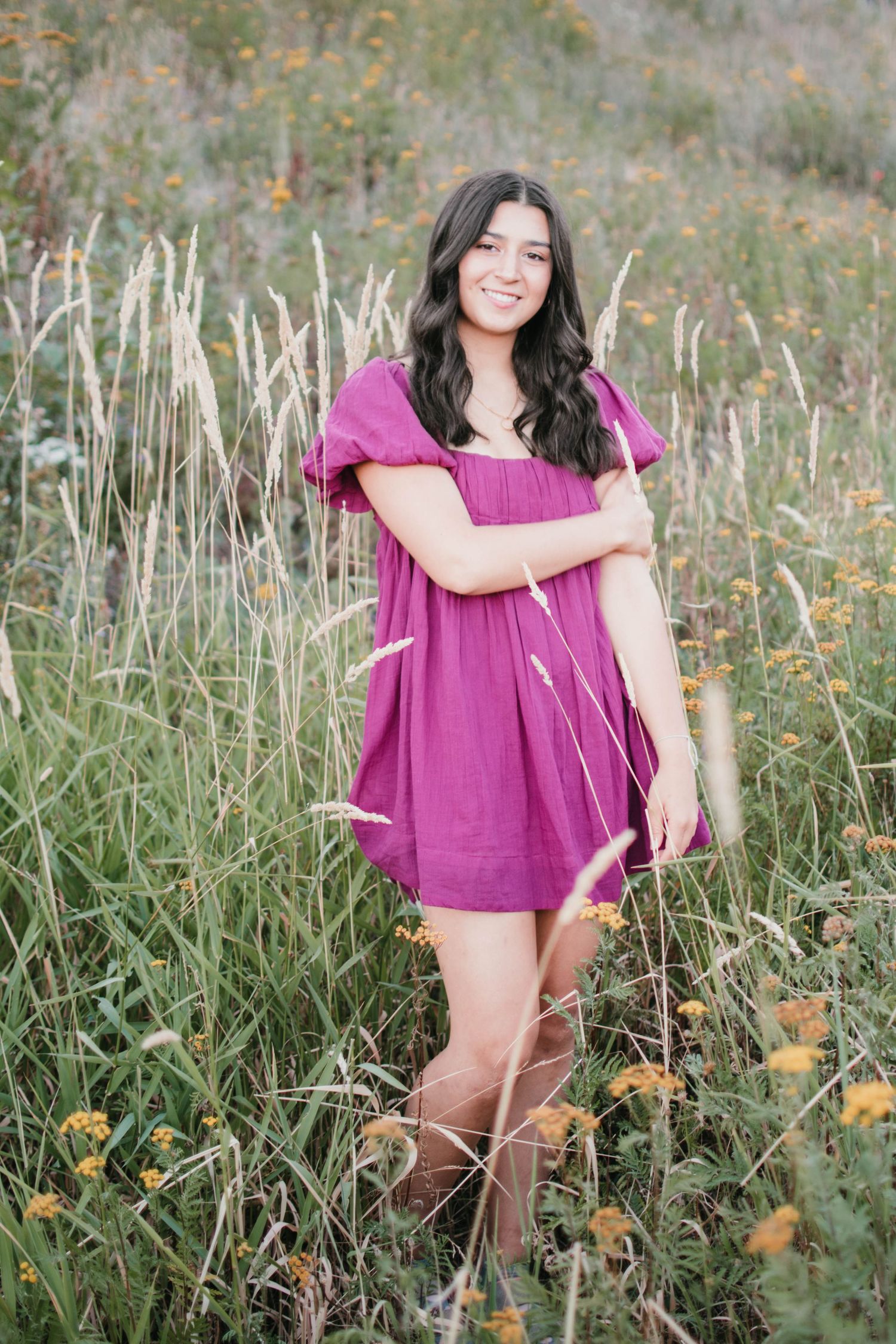 A bright magenta dress stands out against tall grass and wildflowers in a rustic outdoor setting.