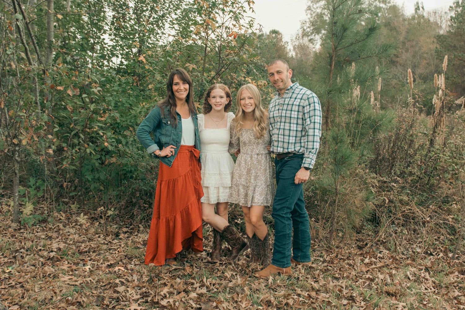 A family in autumn-colored clothing poses together with their dog in a wooded outdoor setting.