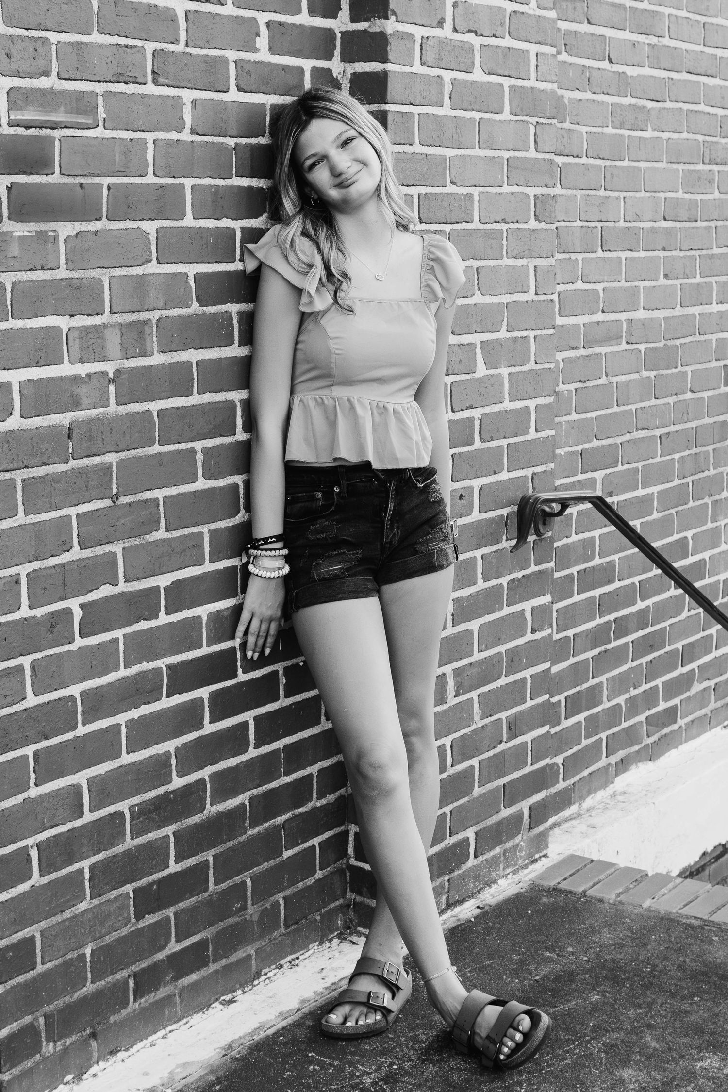 Black and white portrait against brick wall showing casual summer outfit with peplum top and denim shorts.