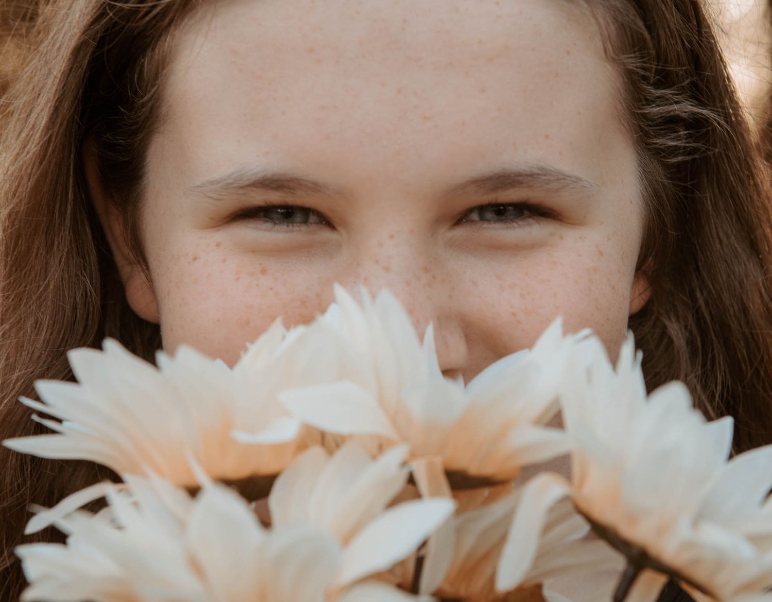 A close-up view of someone smiling while holding white daisy flowers in front of their face.