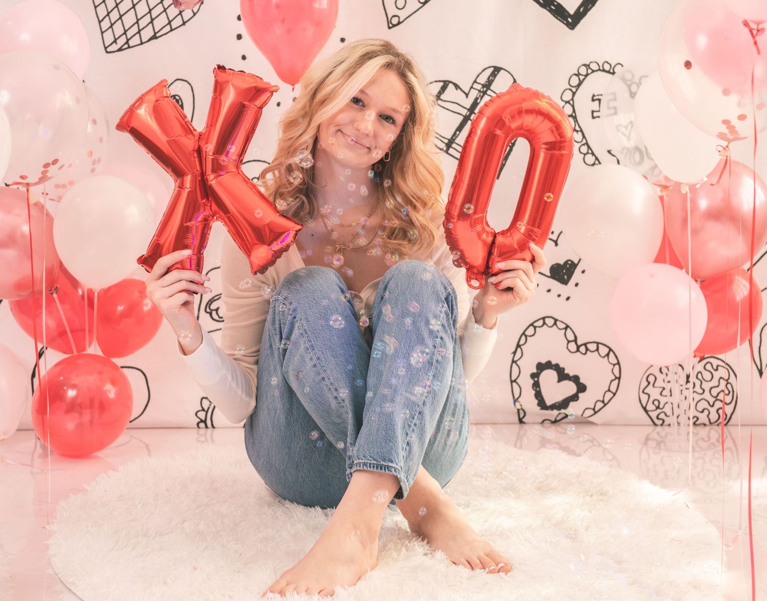 Valentine's photo setup with red XO balloons, pink and white decor, denim casual style against romantic backdrop.