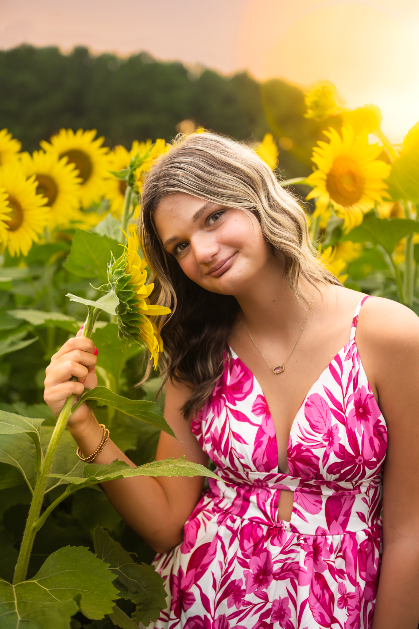 Pink and white floral dress among blooming sunflowers at sunset creating a warm summer portrait aesthetic.