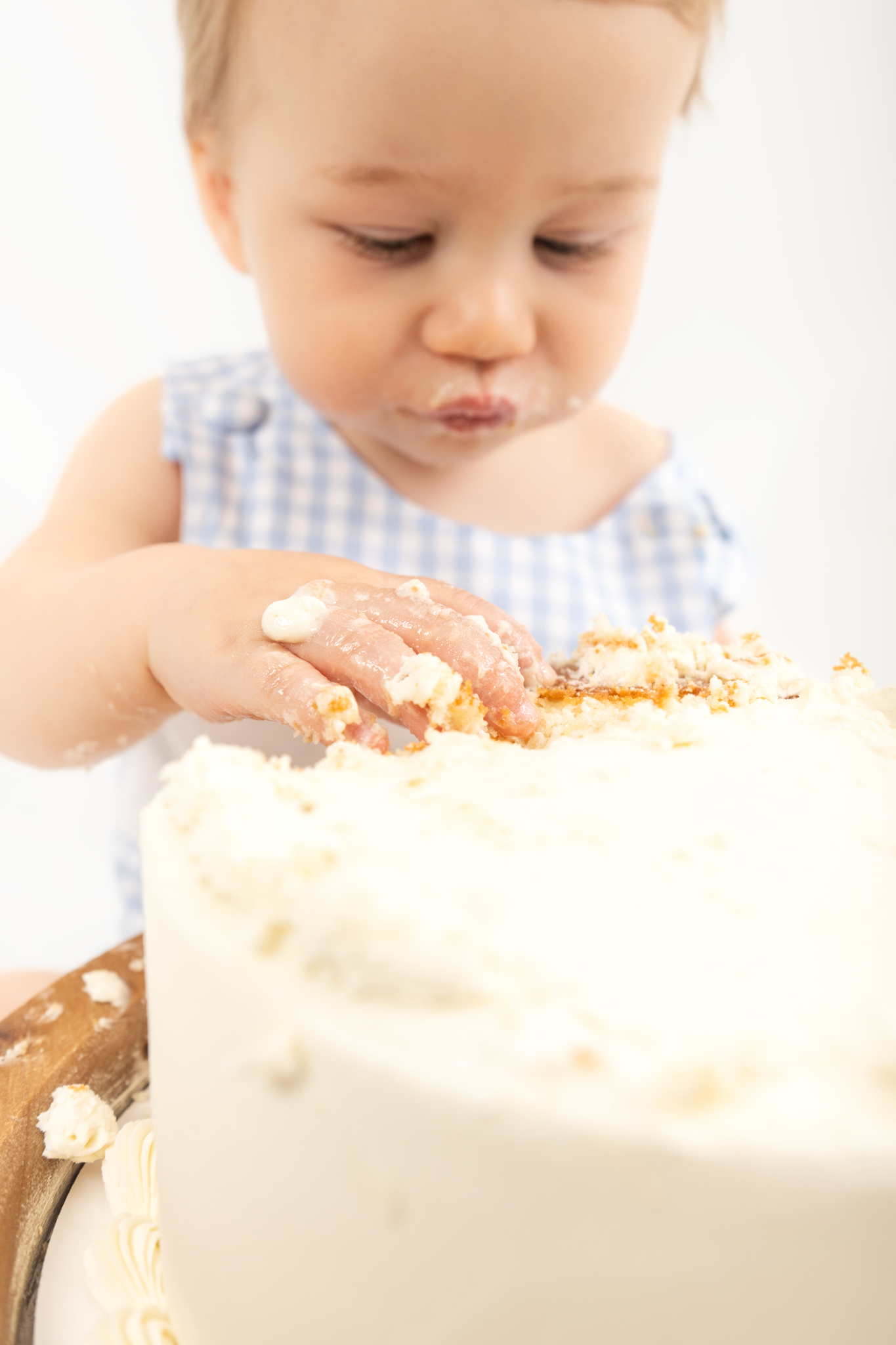 Small hands reach toward a white frosted birthday cake on a rustic wooden surface.