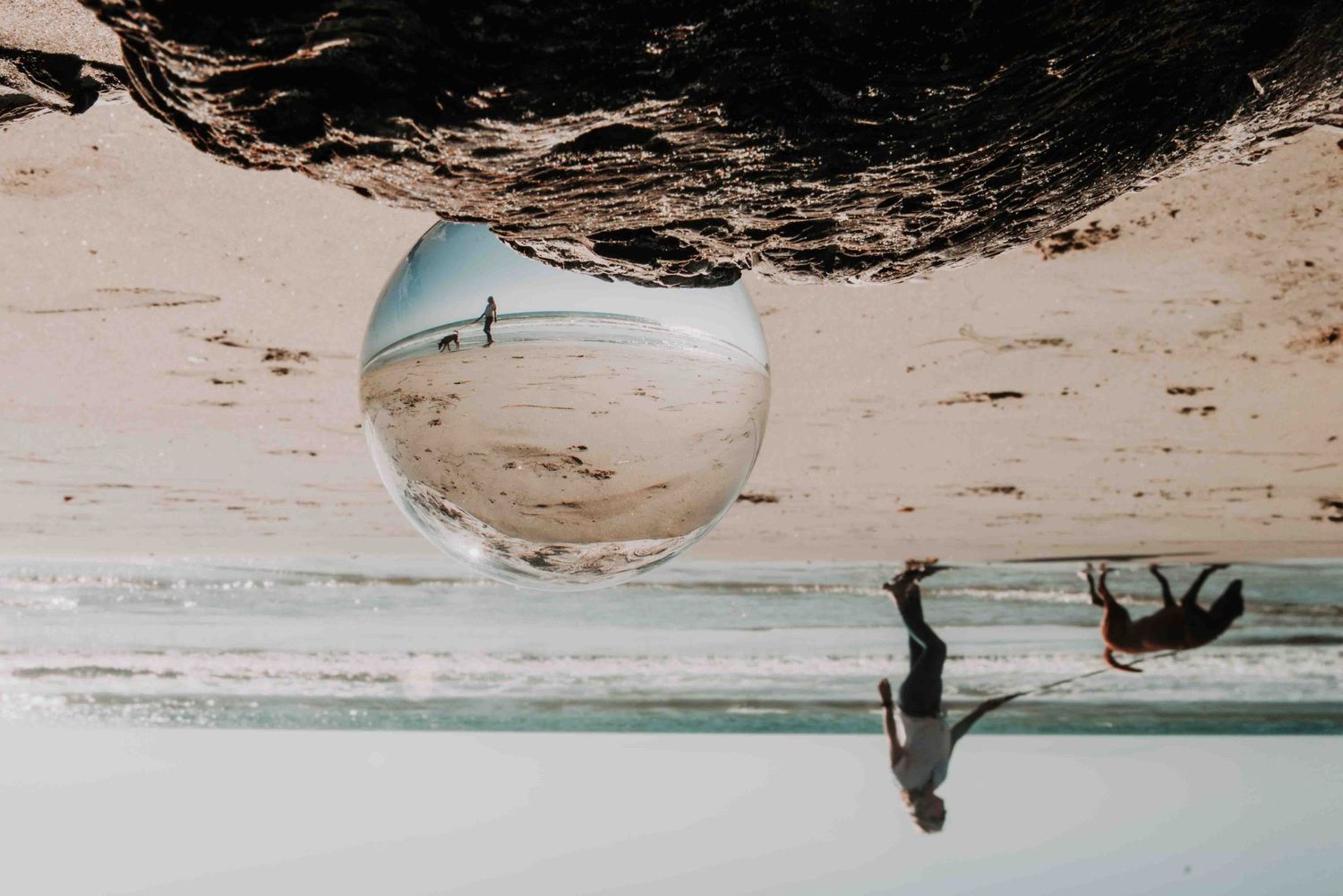 A creative beach scene reflected in a circular mirror showing a silhouette walking along the shoreline at sunset.