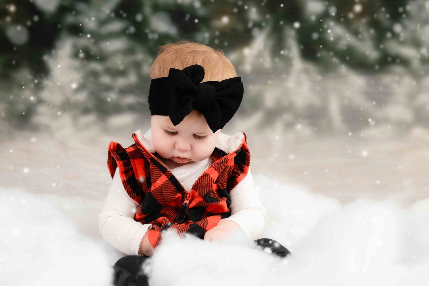 A small figure in a red buffalo plaid outfit sits in fresh winter snow while snowflakes fall around them.