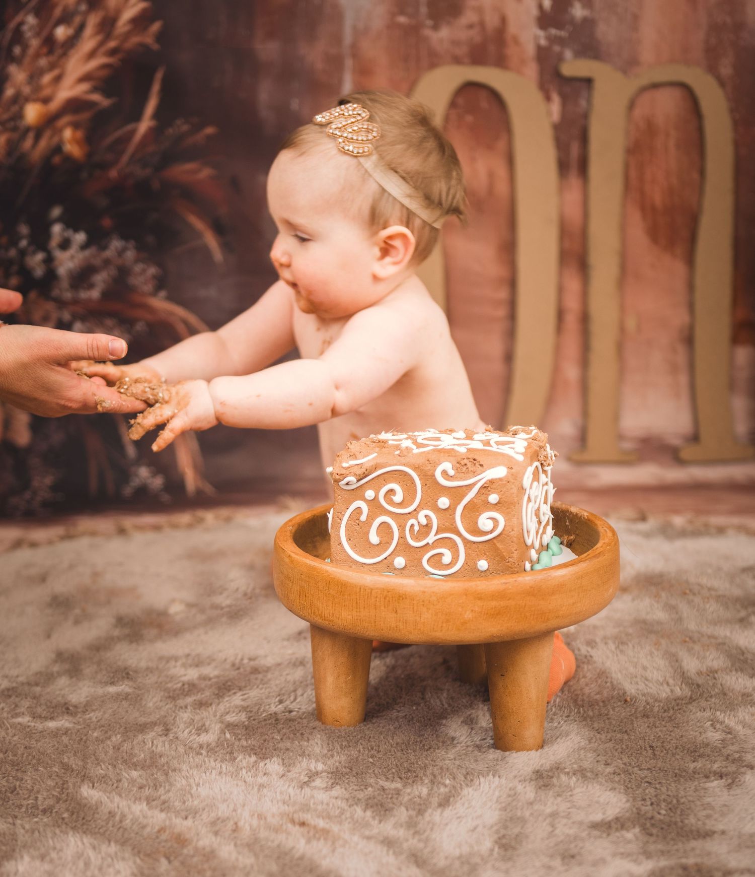 A decorated brown cake on a wooden pedestal with delicate white swirl patterns.