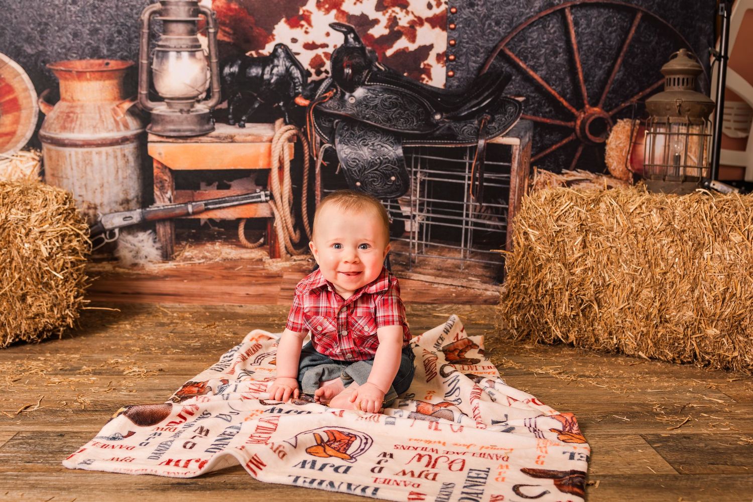 A rustic autumn scene with hay bales, wooden wagon wheel, pumpkins and lantern decorations in warm fall colors.