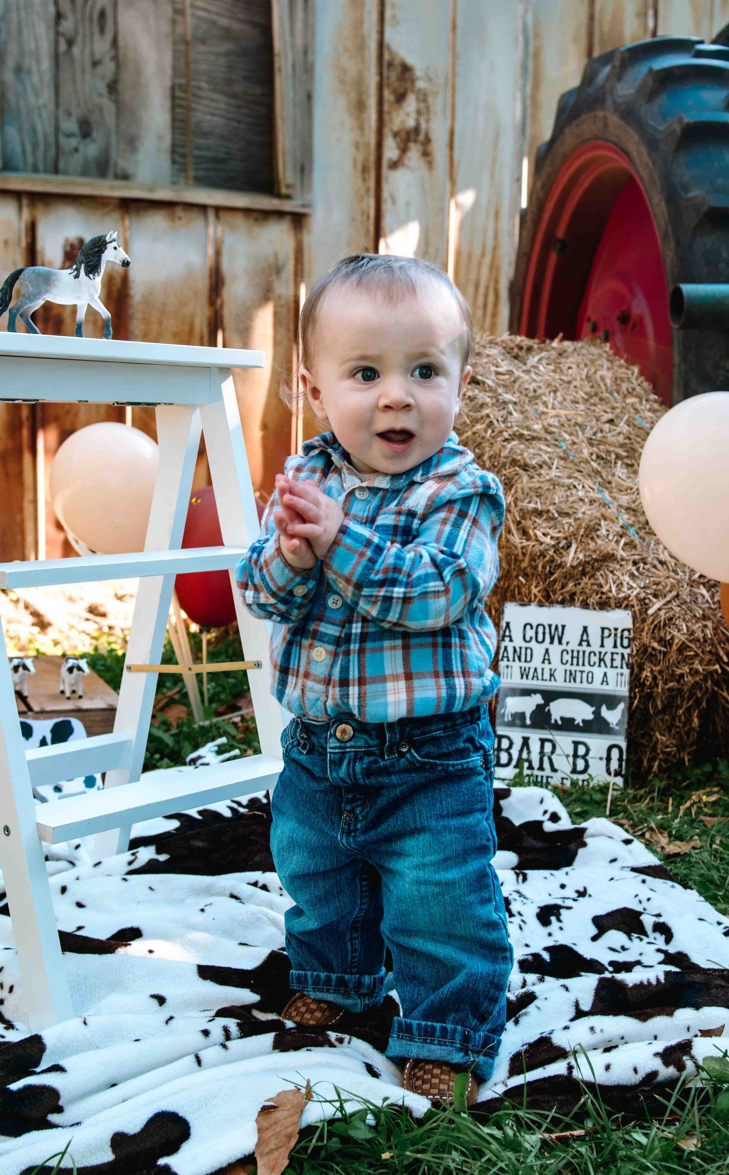 A small child in plaid shirt and jeans stands by a rustic backdrop with hay bales and vintage farm decor.