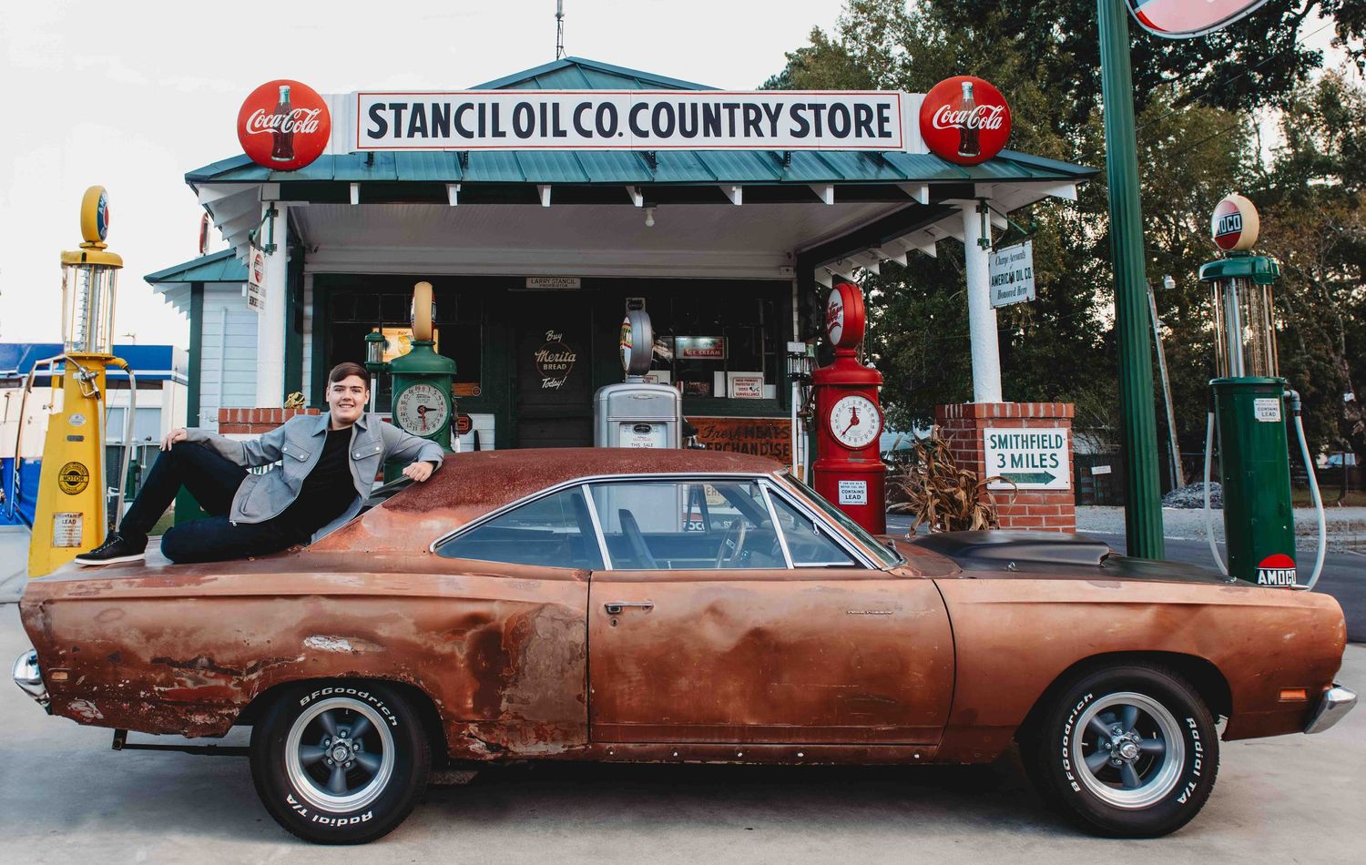 High school graduate on top of classic rusty muscle car in front of vintage rustic Stancil Oil Co country store in Smithfield, NC.