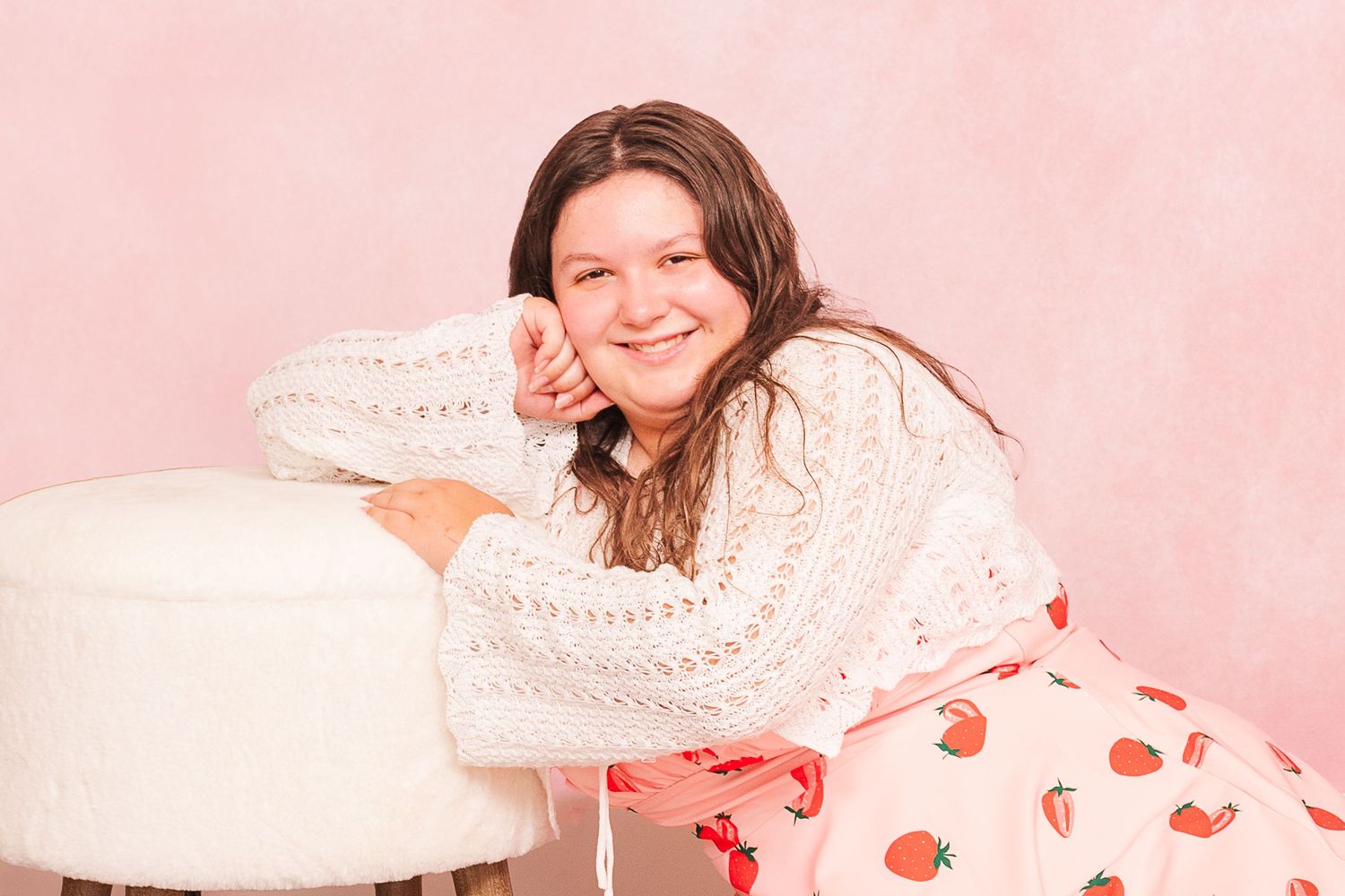 A person in a white knit sweater and red heart print pajamas lounging on a pink background.