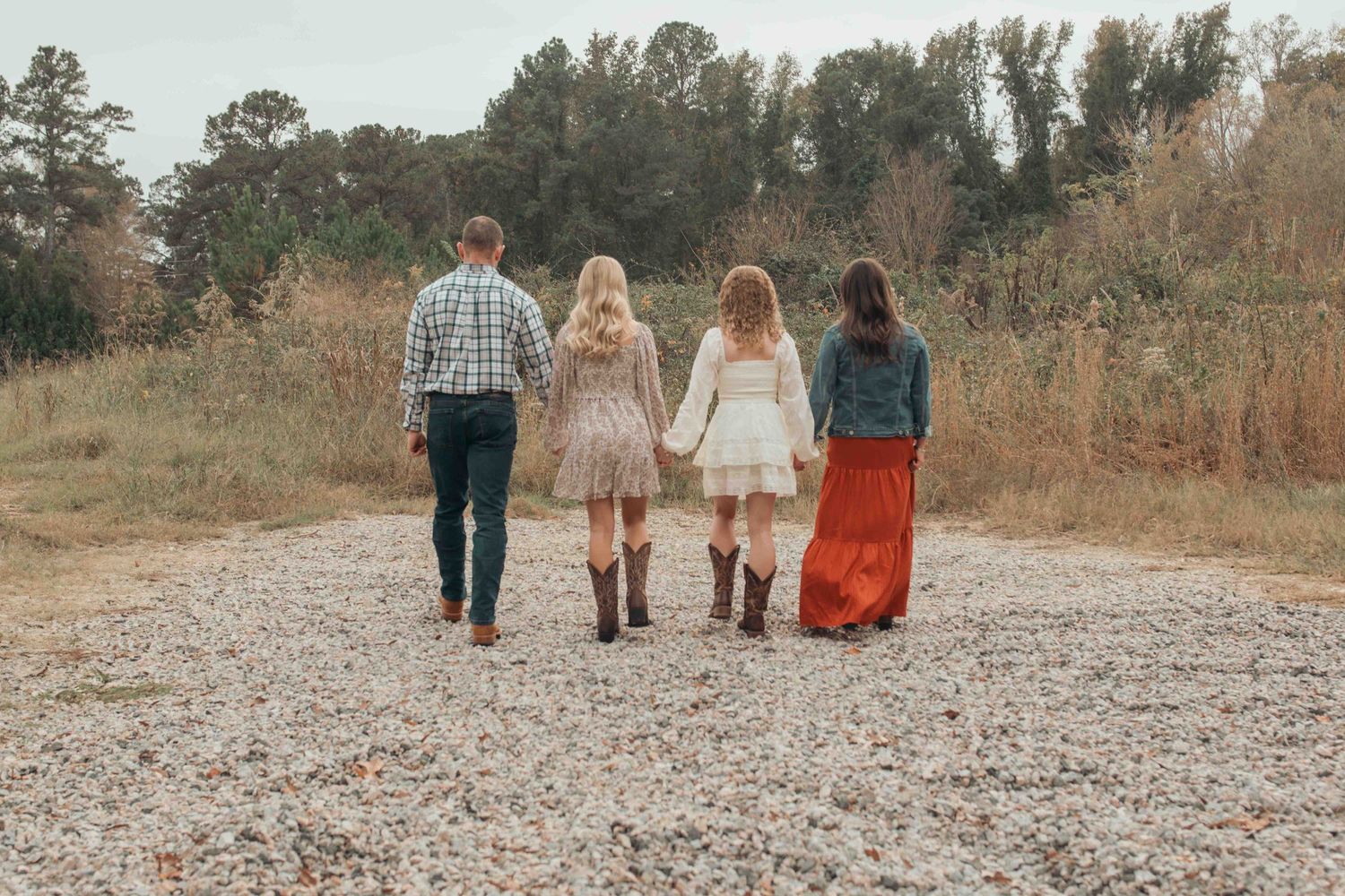 Four friends walk away together down a gravel path surrounded by autumn foliage in the countryside.