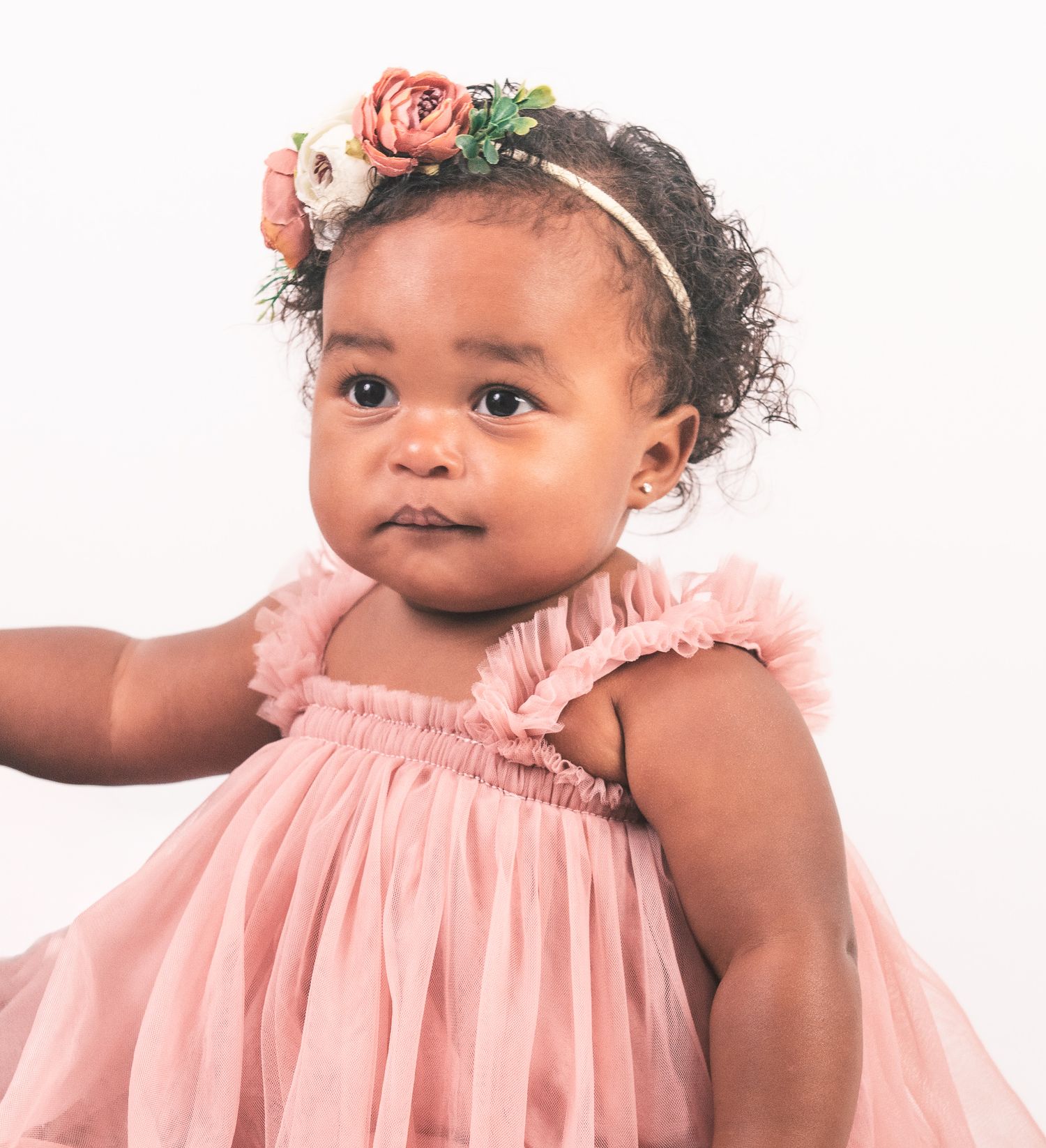 Sweet baby wearing pink ruffled dress and floral crown against white background.