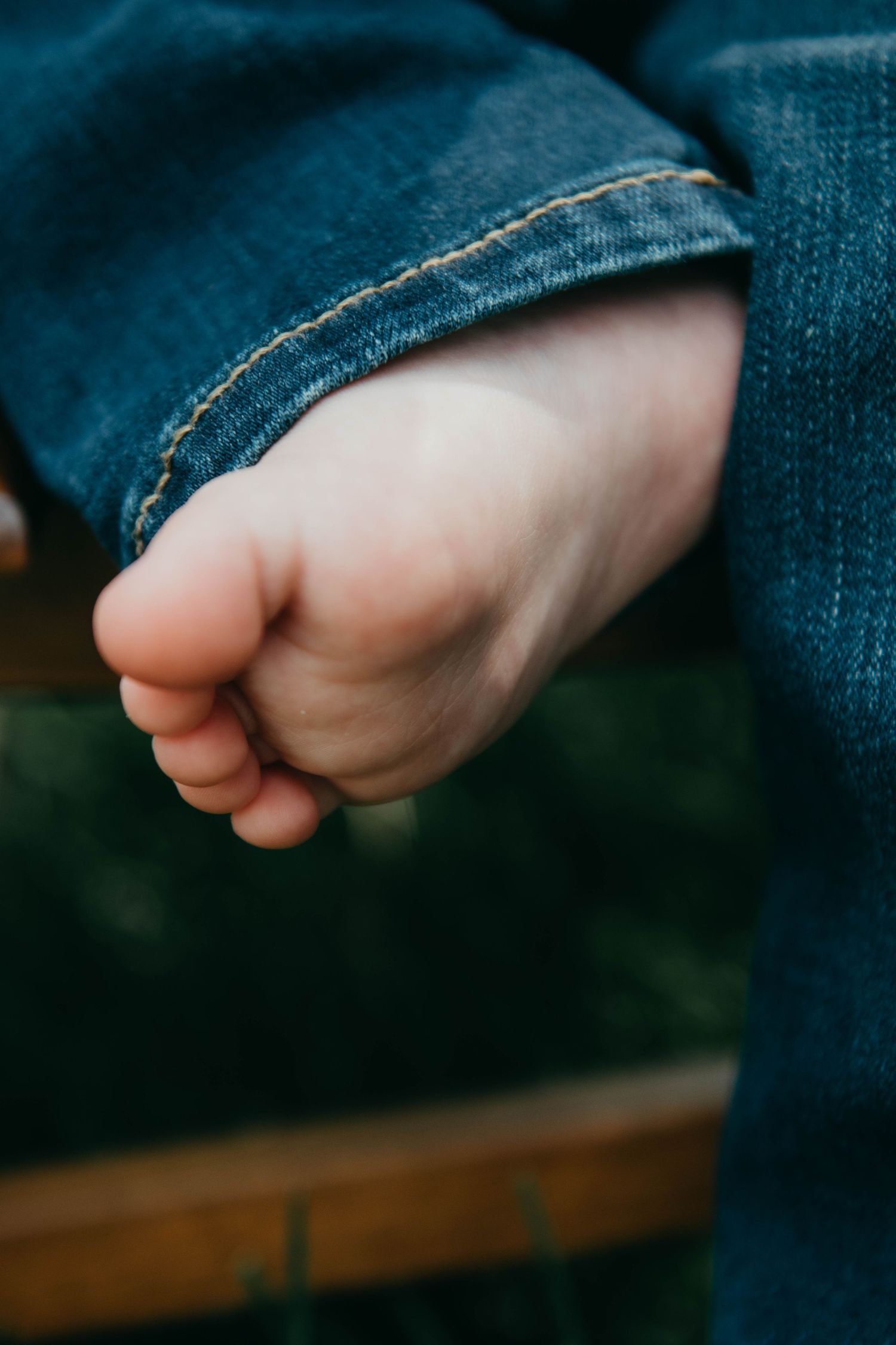 Close-up of a tiny bare foot peeking out from blue denim jeans against a blurred background.