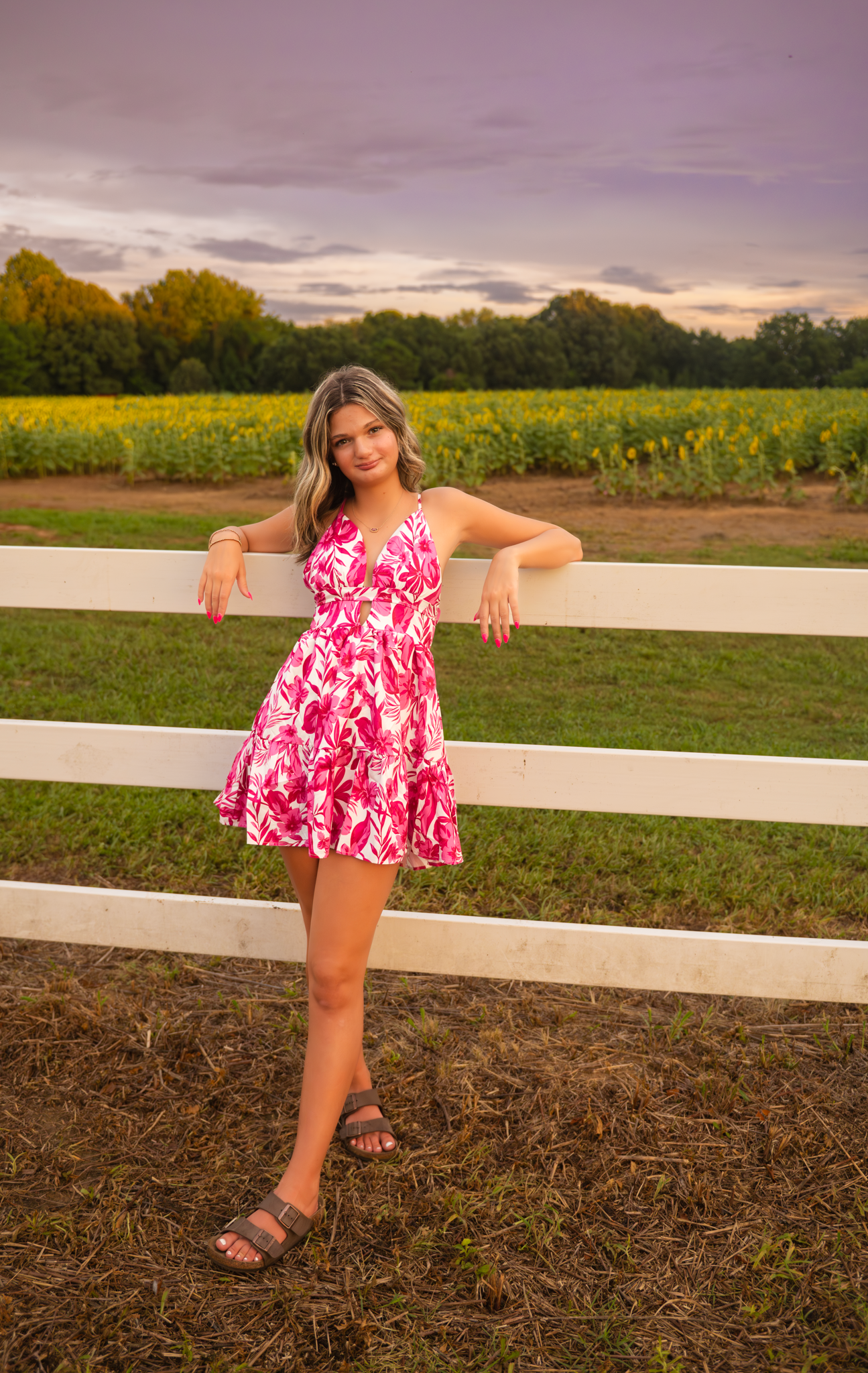 Pink and white floral dress worn in a summer field with white fence and wildflowers at sunset.