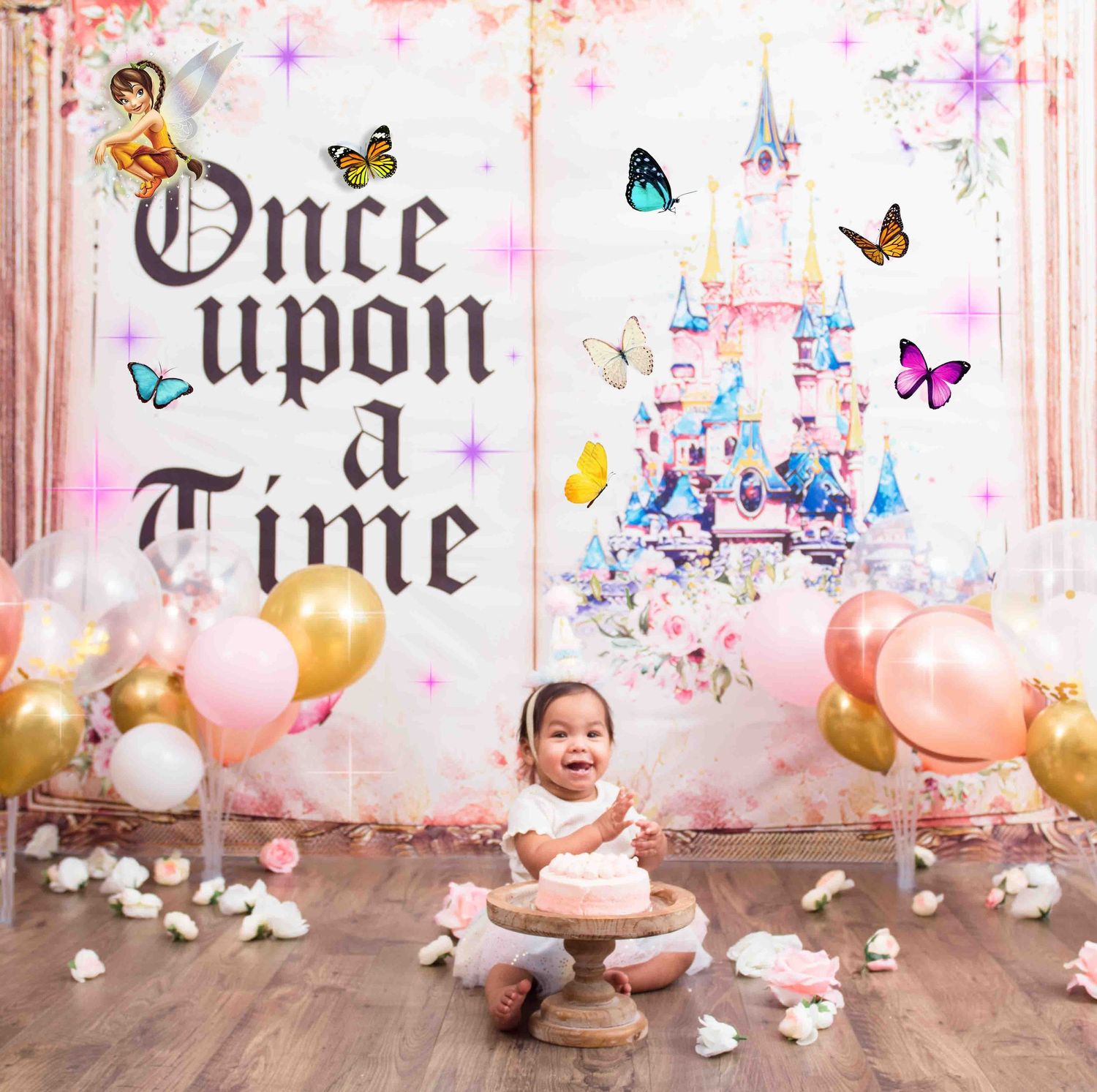 Fairy tale themed baby photo setup with pink balloons, butterflies, and a castle backdrop against a rustic wall.
