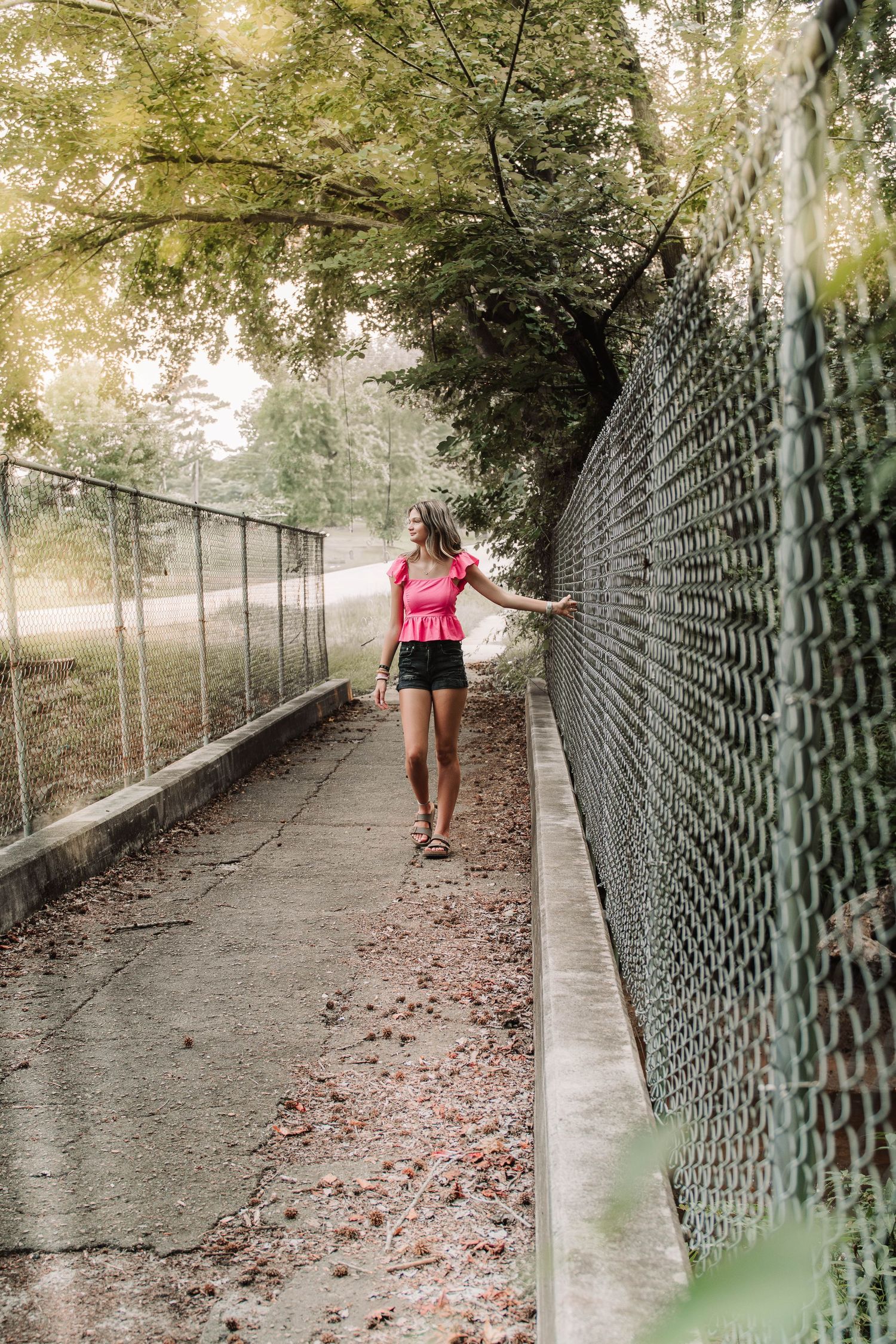 Athletic figure in pink top walking along a path between chain link fences on a misty morning.