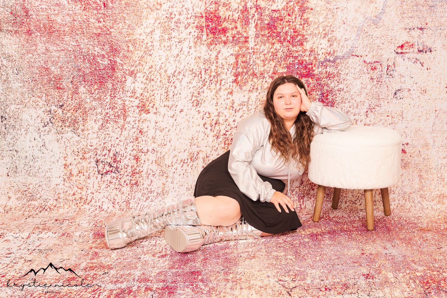 Lifestyle portrait against pink textured backdrop with white ottoman and cozy winter fashion styling.
