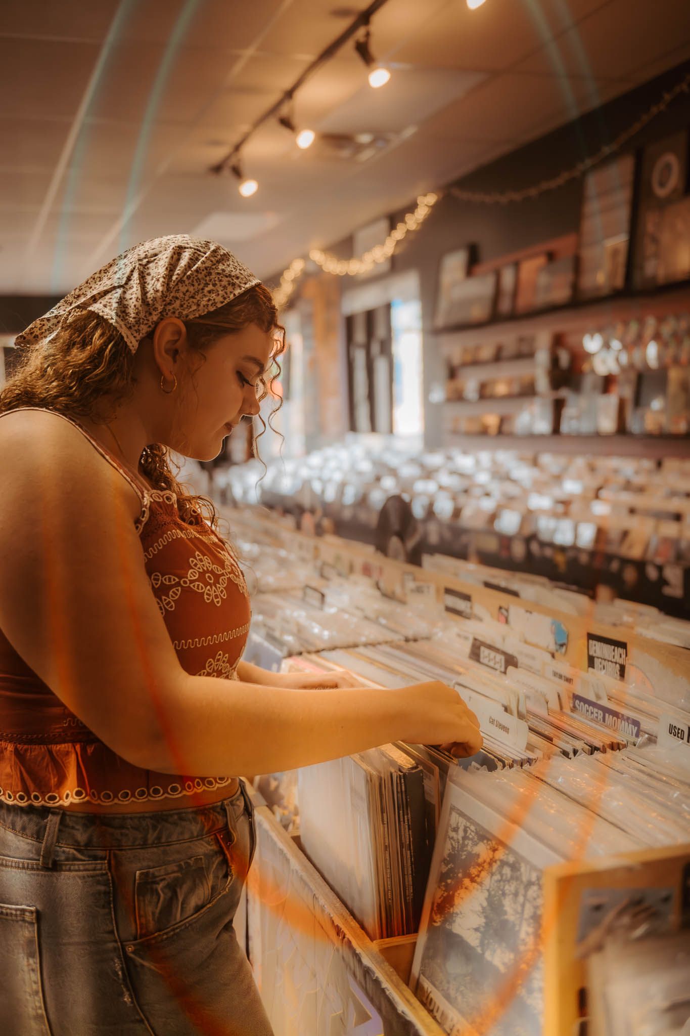 Person browsing through vinyl records in a music store with warm lighting and shelves of albums in the background.