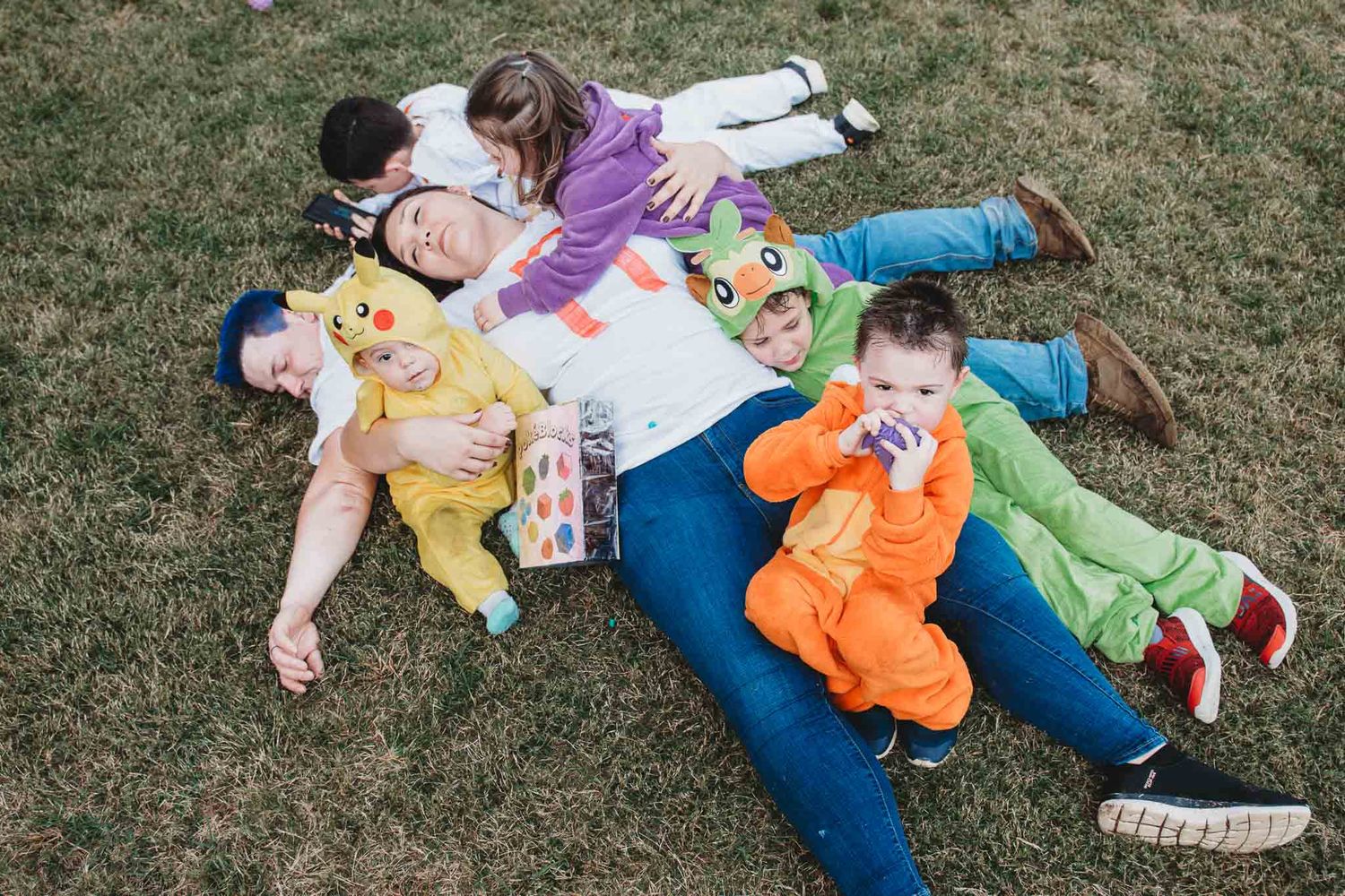 Group of people lying in a star formation on grass while reading books in colorful casual clothing.