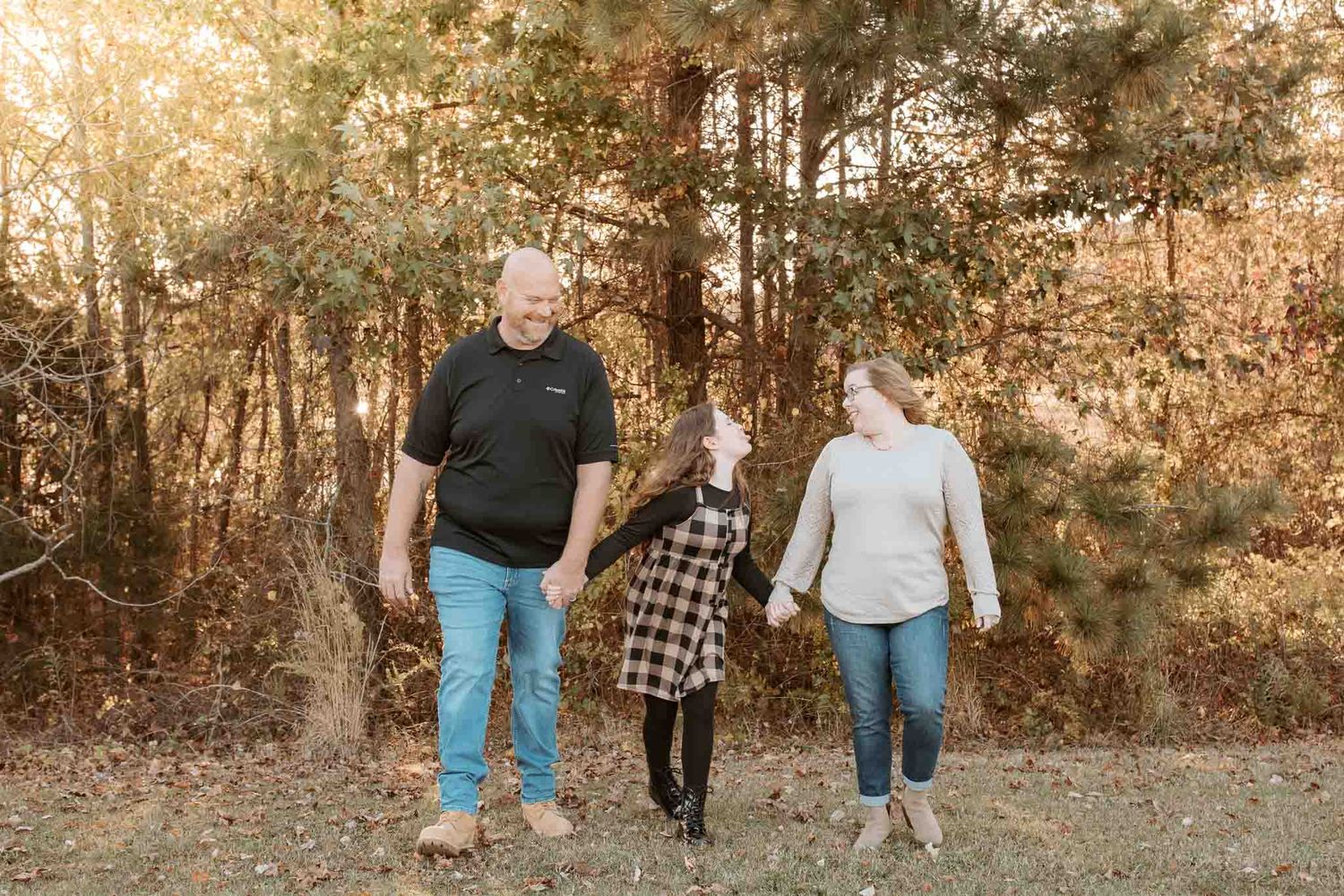 Three people holding hands while walking down a forest path during golden sunset hours in autumn.