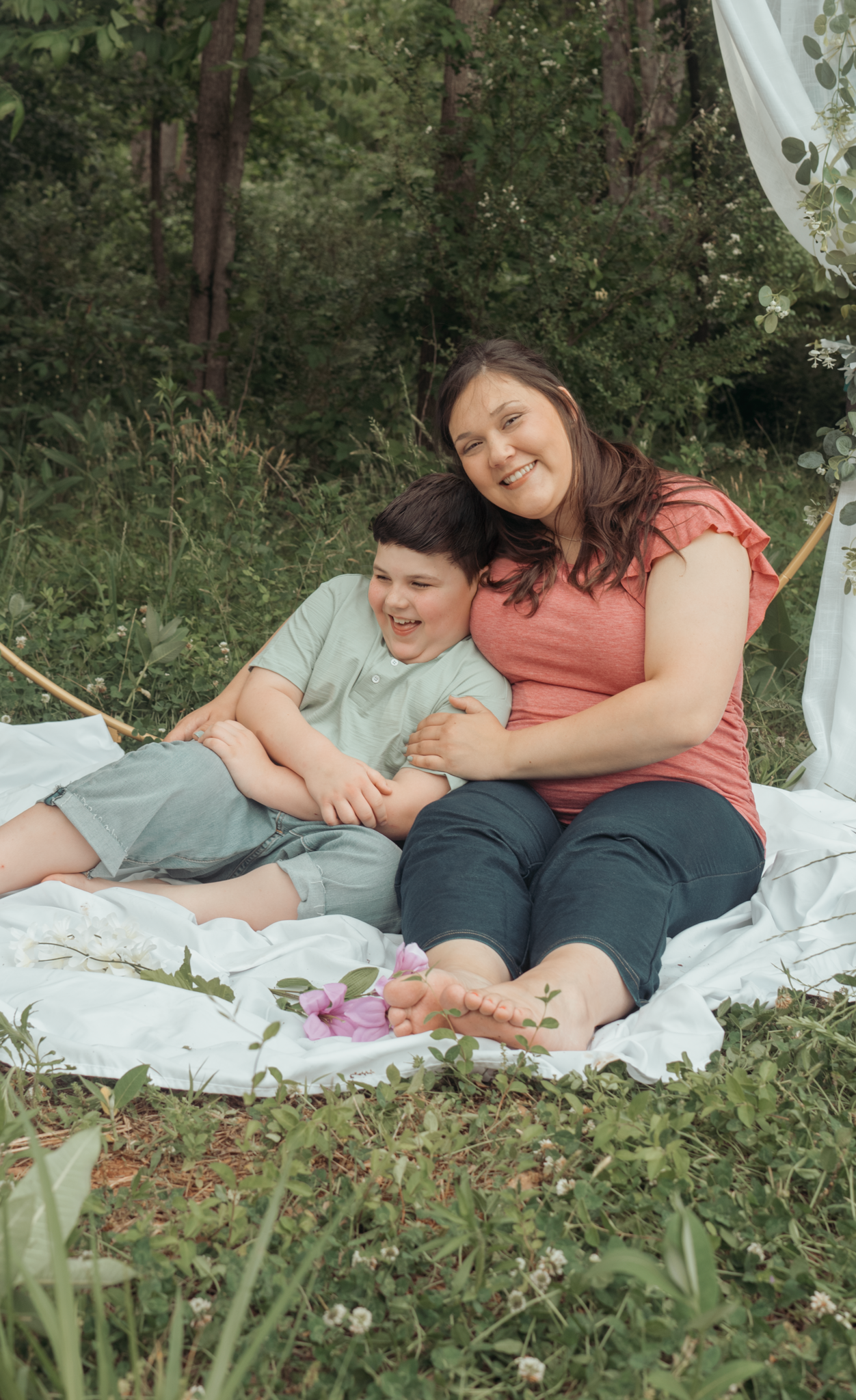 Two people share a joyful moment while relaxing on a white blanket outdoors surrounded by greenery.