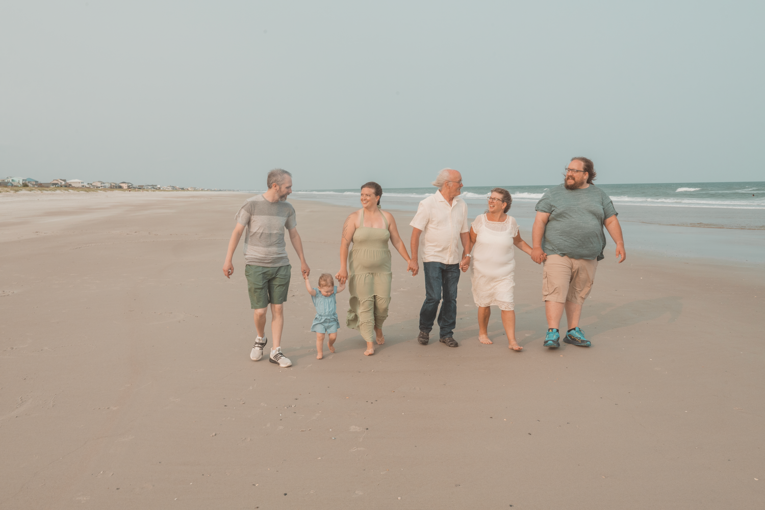 A group walks together along a sandy beach during sunset with waves and ocean visible in the background.