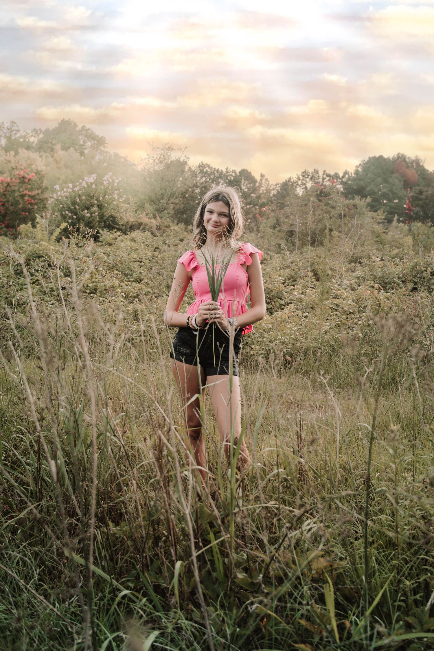 A portrait in a dreamy meadow at golden hour featuring a coral top and dark shorts ensemble.