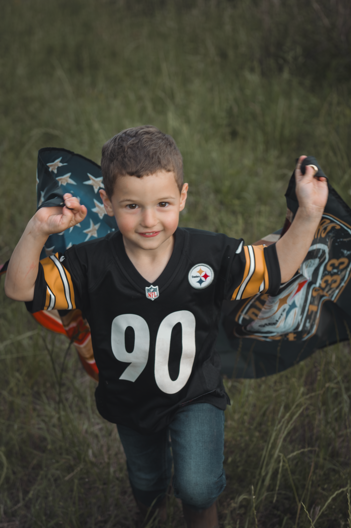 Young sports fan wearing a Pittsburgh Steelers #90 jersey holds up a waving flag in an outdoor field setting.