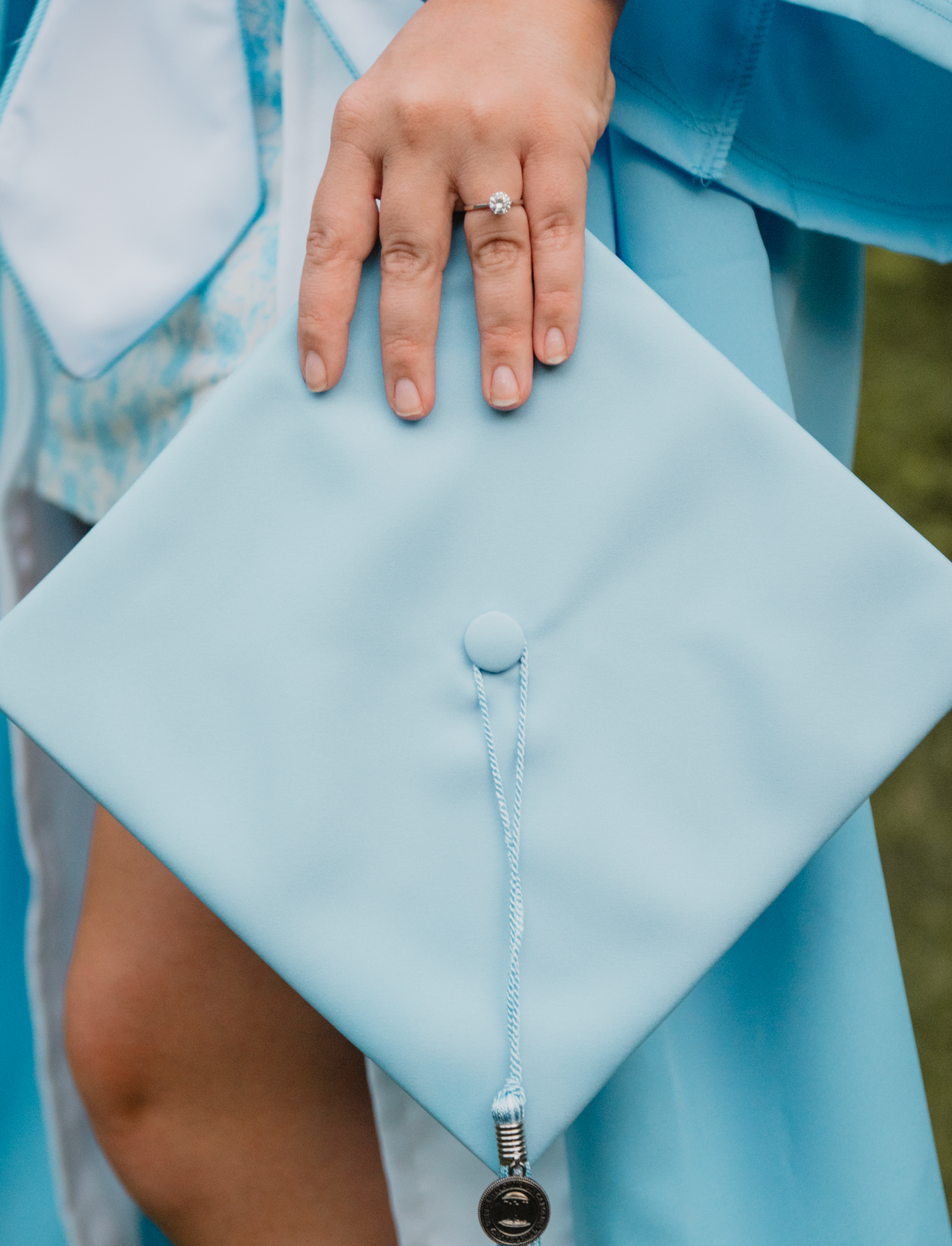 A close-up view of light blue graduation robes with hands adjusting details and tassel decorations against a bright background.