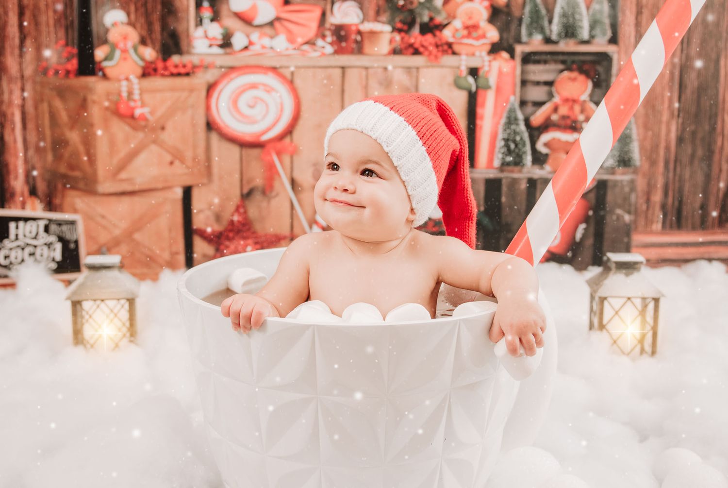 Sweet holiday scene with baby in white outfit against rustic wooden backdrop with candy cane decorations and warm lighting.