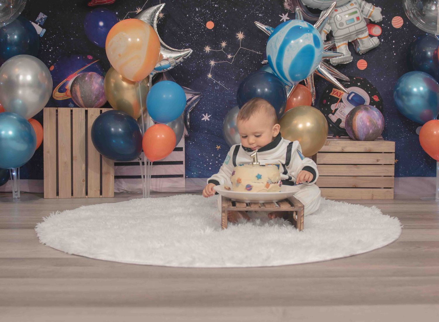 Whimsical space-themed party setup with wooden crates and colorful balloons for child's first birthday cake smash in Smithfield, NC