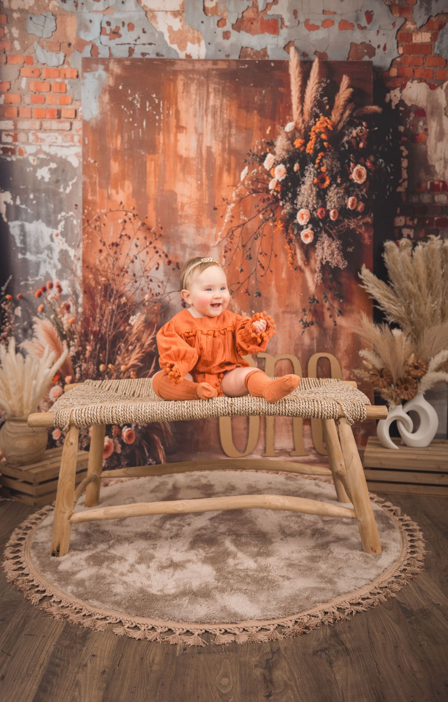 A rustic autumn scene with dried flowers and pampas grass surrounding a wooden bench with orange accents.